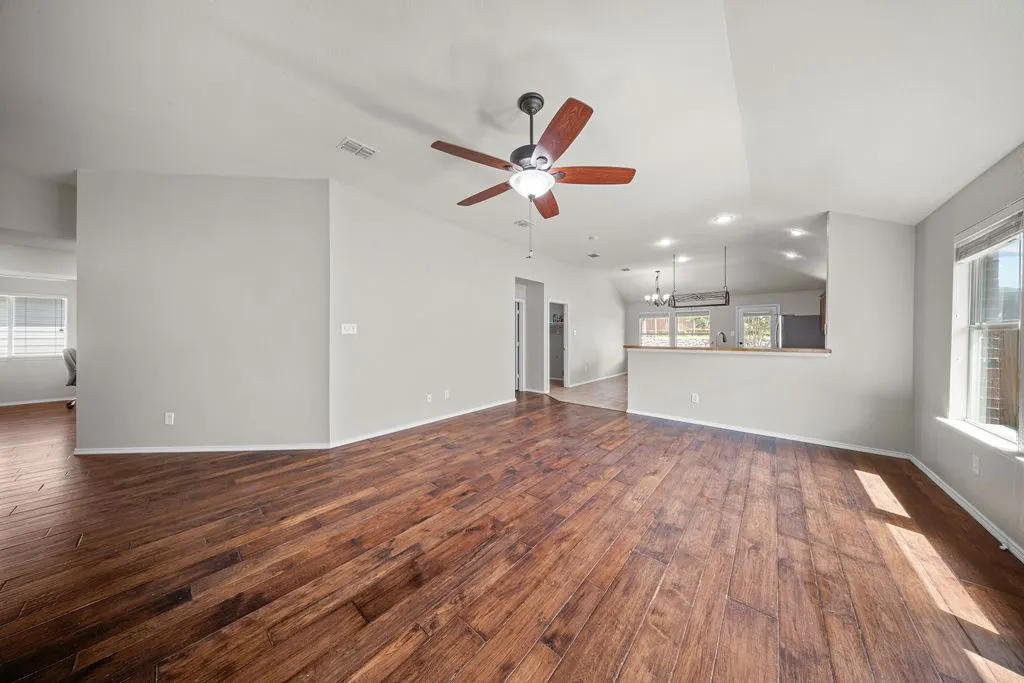 Spacious living area featuring wood-finish flooring, vaulted ceilings, and a ceiling fan with integrated lighting
