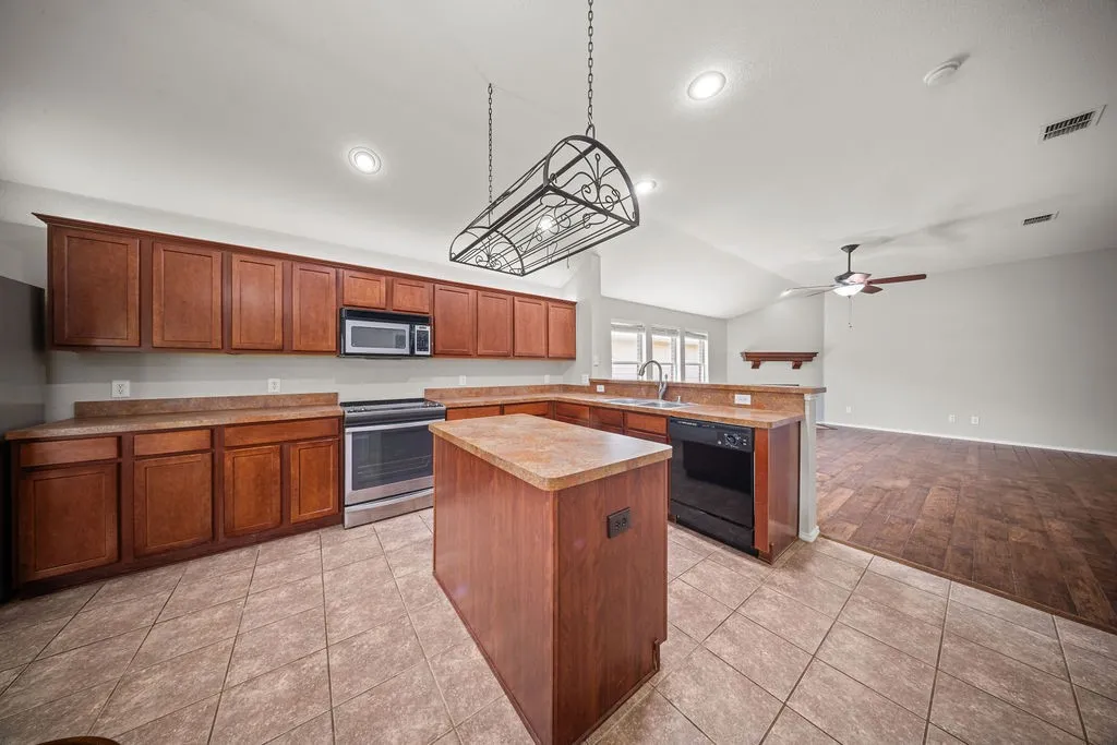 Spacious kitchen featuring a large island, wood-finish cabinetry, stainless steel range and microwave, tile flooring, and recessed lighting