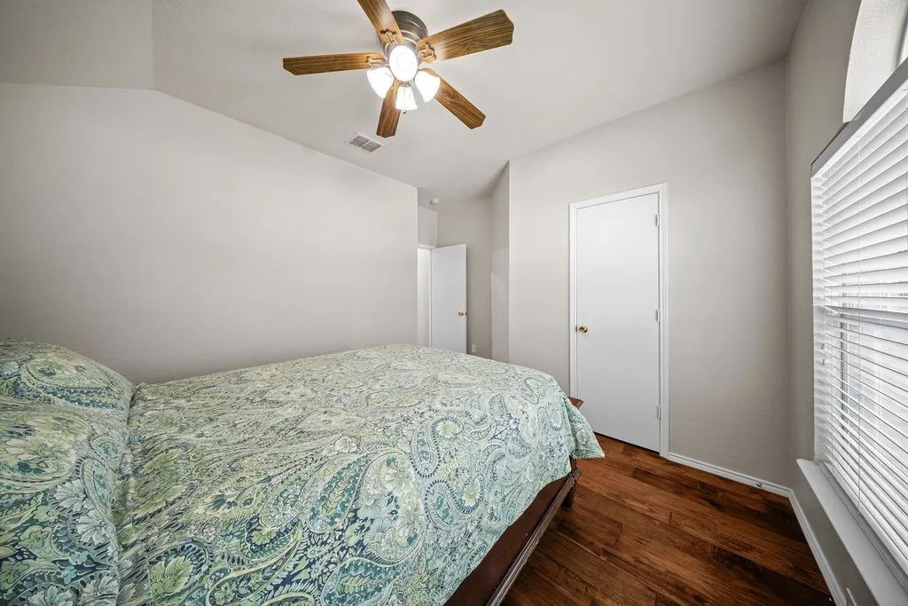 Bedroom featuring wood-finish flooring, a ceiling fan with integrated lighting, and multiple doors with brass hardware