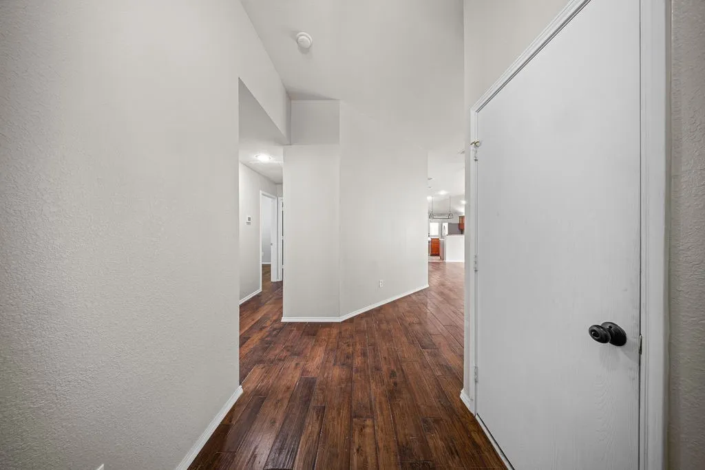 Hallway featuring wood-finish flooring, light grey painted walls, white trim, and a white interior door with a black knob