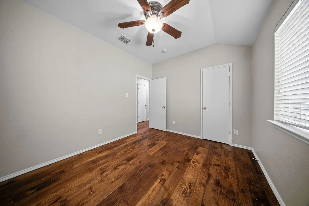 Spacious room featuring rich wood-finish flooring, light gray walls, and a vaulted ceiling