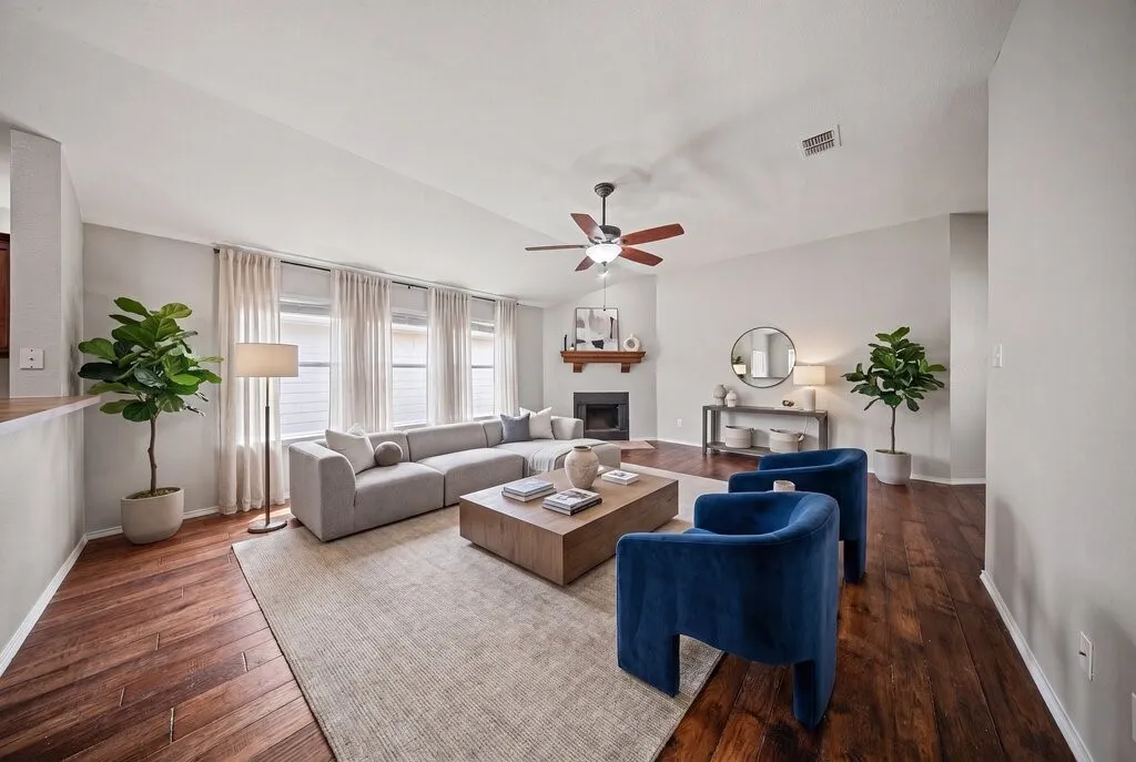 Spacious living area featuring vaulted ceilings, wood-finish flooring, and a corner fireplace with a wooden mantel