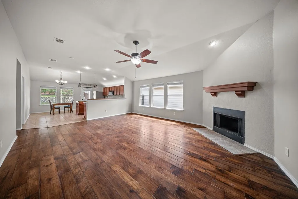 Spacious living area featuring wood-finish flooring, a vaulted ceiling, and a fireplace with a wood mantle