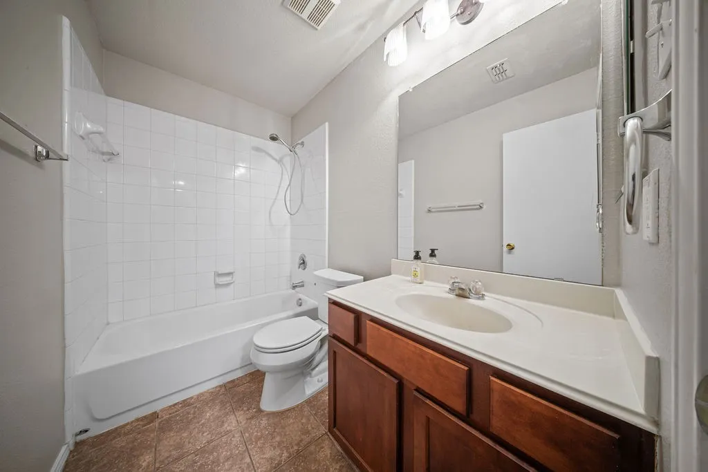 Bathroom featuring a bathtub with subway tile surround, a toilet, a vanity with a white countertop and integrated sink, and an overhead mirror with vanity lighting