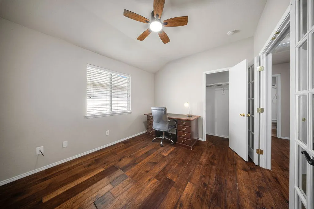 Spacious room featuring wood-finish flooring, vaulted ceilings, and a ceiling fan