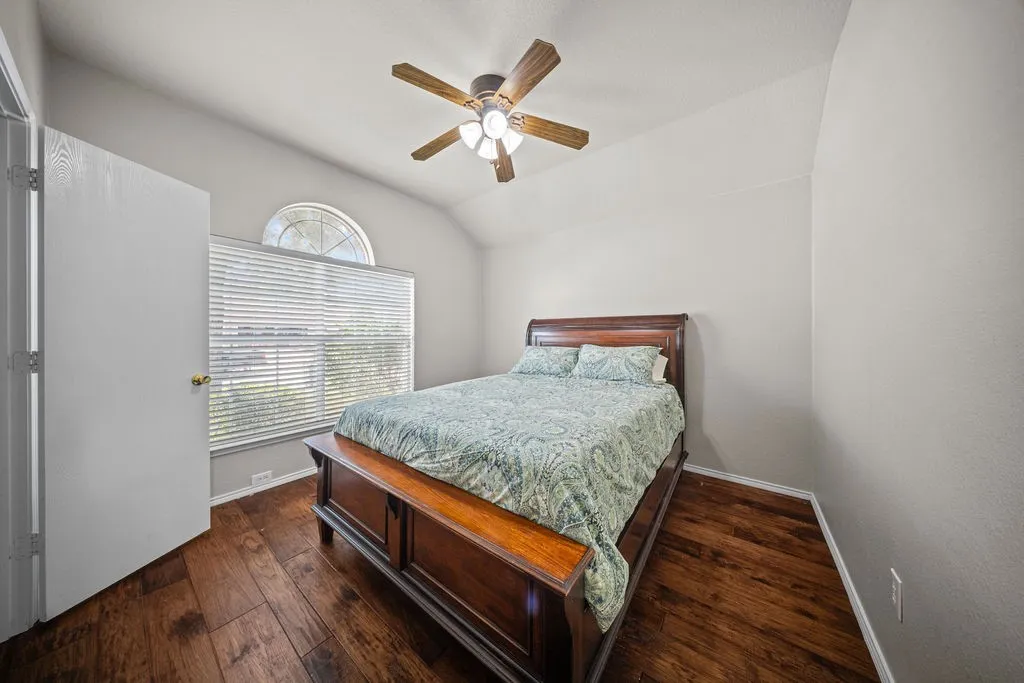 Vaulted ceiling room featuring wood-finish flooring, a semi-circular transom window, and a ceiling fan with integrated lighting