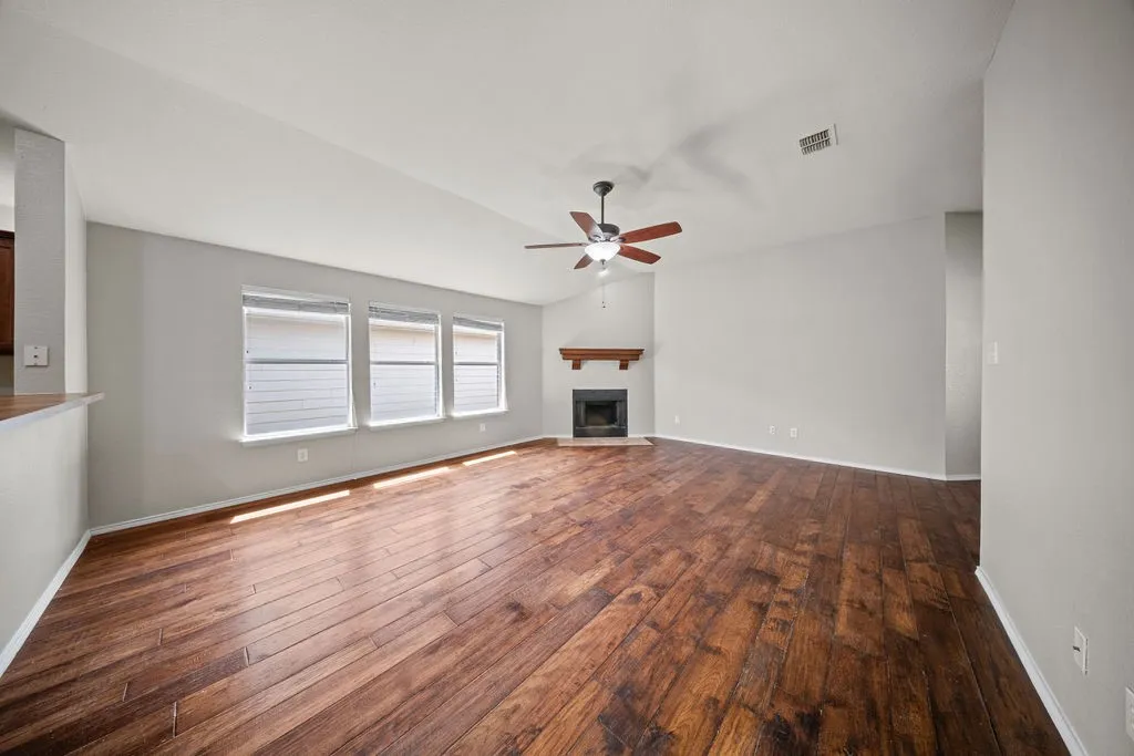 Spacious living area featuring wood-finish flooring, vaulted ceilings, and a corner fireplace with a wood mantel