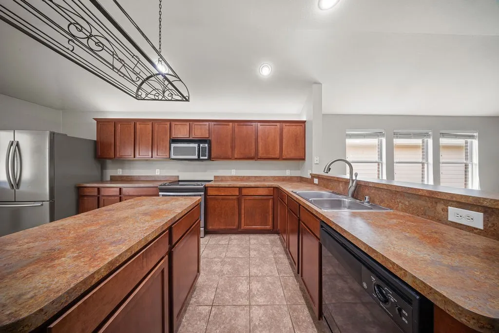 Kitchen featuring a central island, wood cabinetry, stainless steel refrigerator, and a double basin sink