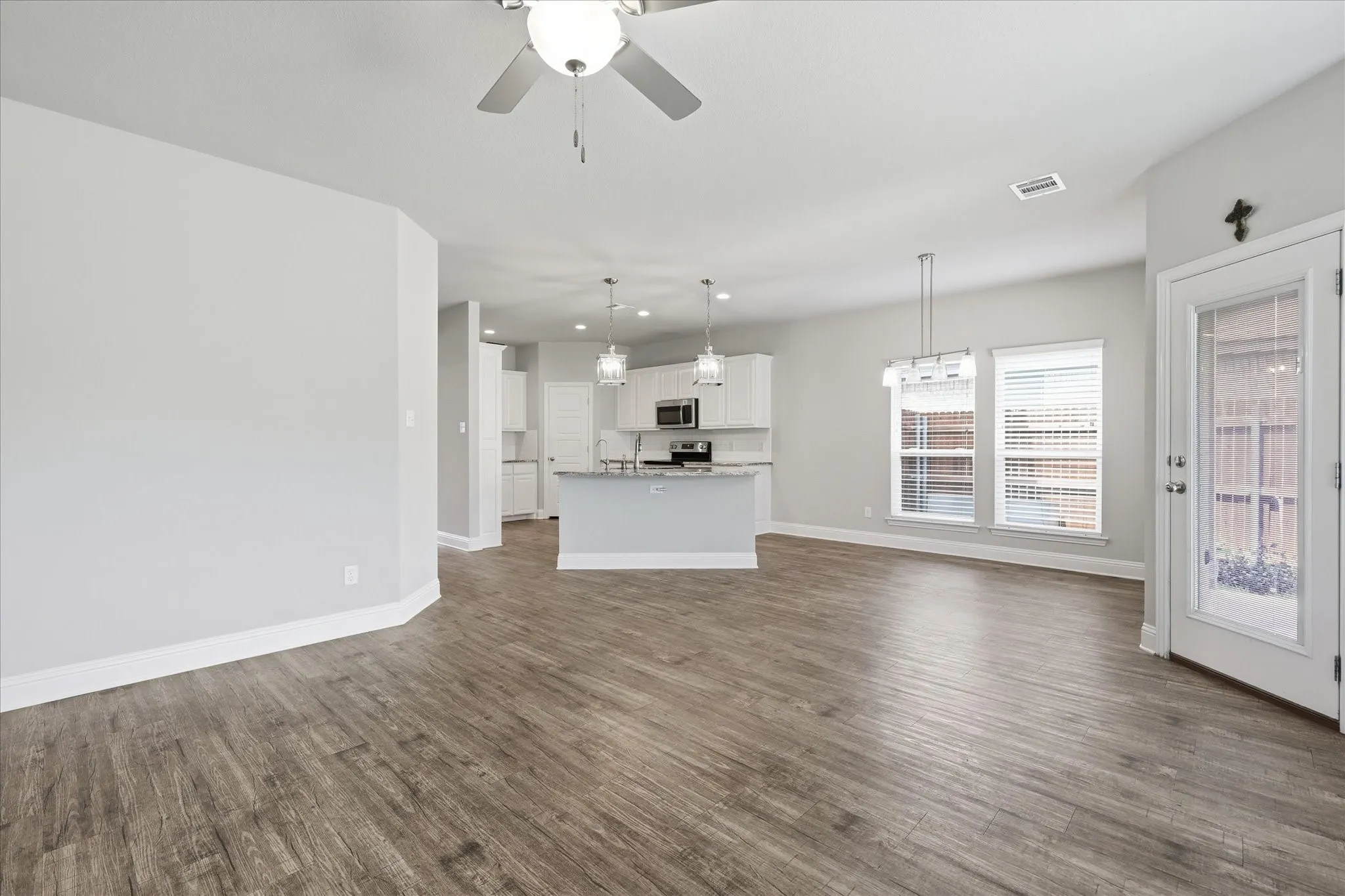 Open-concept living area featuring wood-finish flooring, a contemporary ceiling fan, and a kitchen with white cabinetry, stainless steel appliances, and a central island with pendant lighting