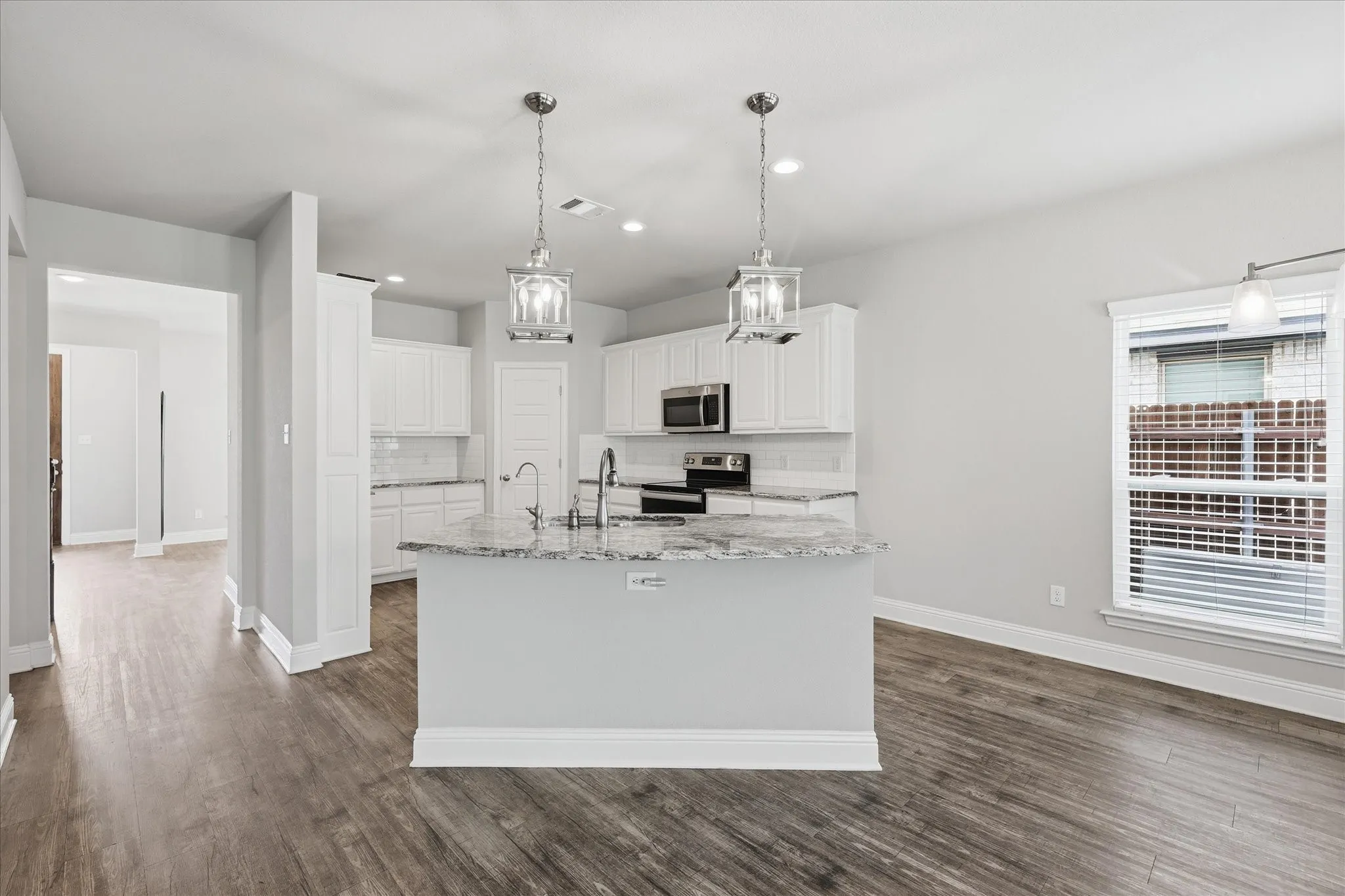 Designed for everyday living and entertaining, this open-concept kitchen features a large granite island, stainless steel appliances, white cabinetry, and abundant workspace at the heart of the home.