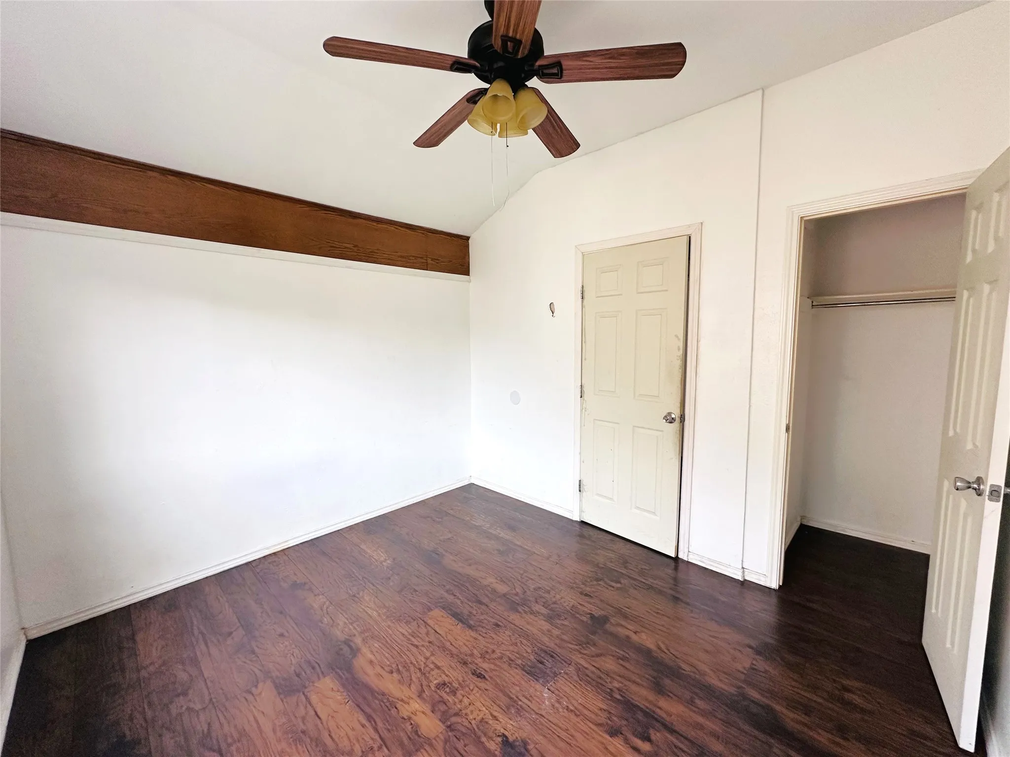 Room featuring wood-finish flooring, a vaulted ceiling, an exposed wood beam, a ceiling fan with integrated lighting, and a closet with a bifold door