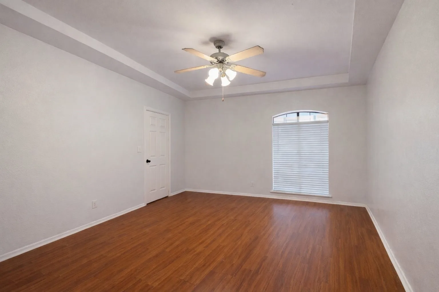 Room featuring wood-finish flooring, a tray ceiling, and a ceiling fan with integrated lighting