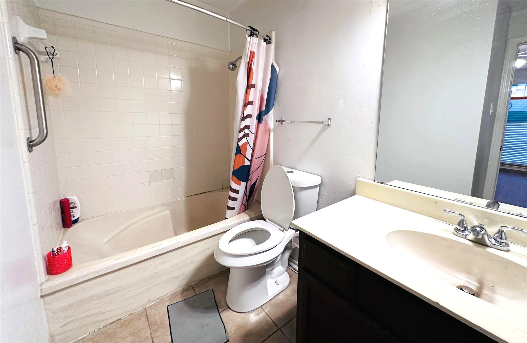 Bathroom featuring a combination shower and tub with white tile surround, a built-in grab bar, a toilet, and a vanity with an integrated sink and mirror