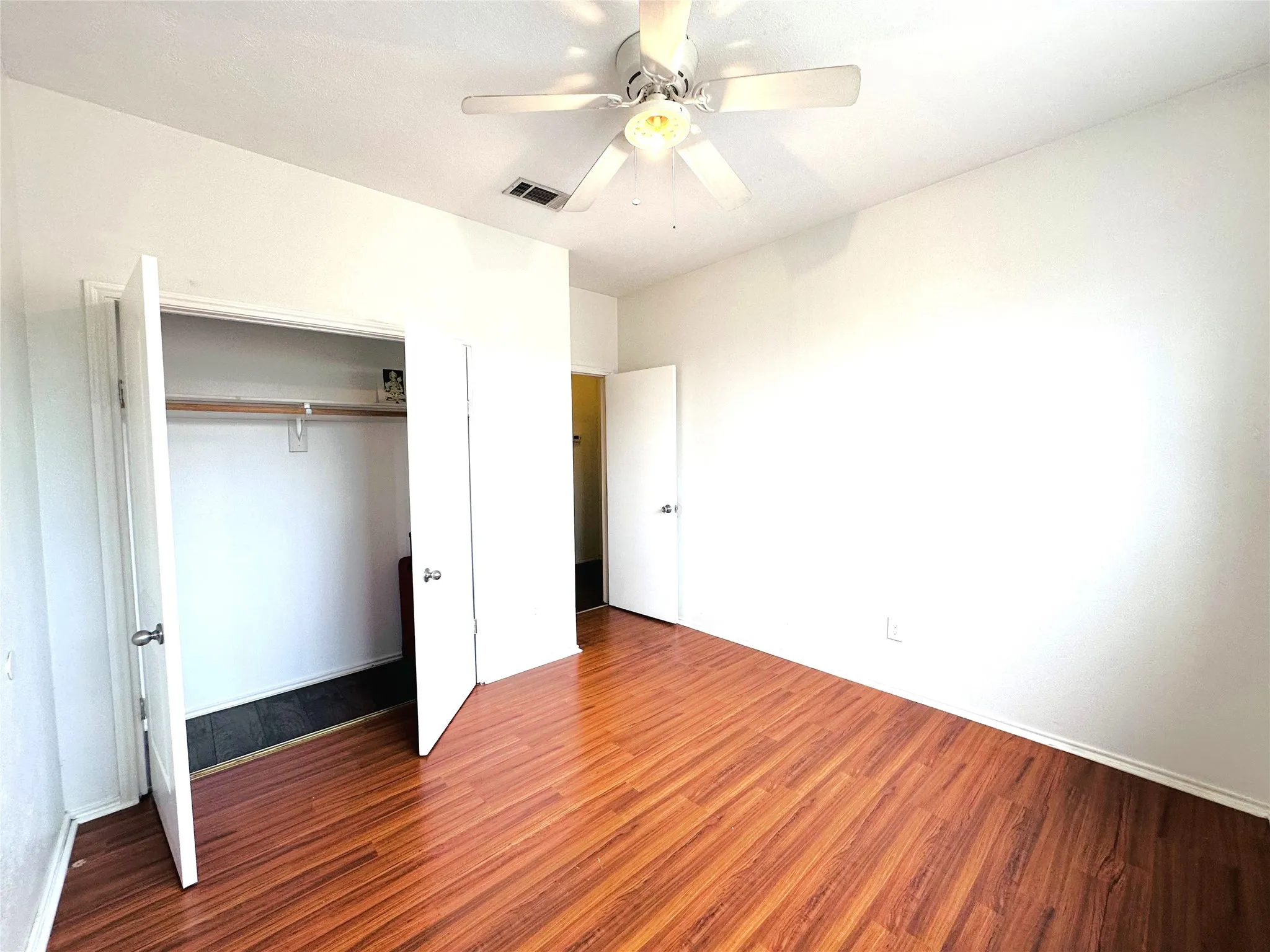 Room featuring wood-finish flooring, a ceiling fan with integrated lighting, and a closet with bifold doors