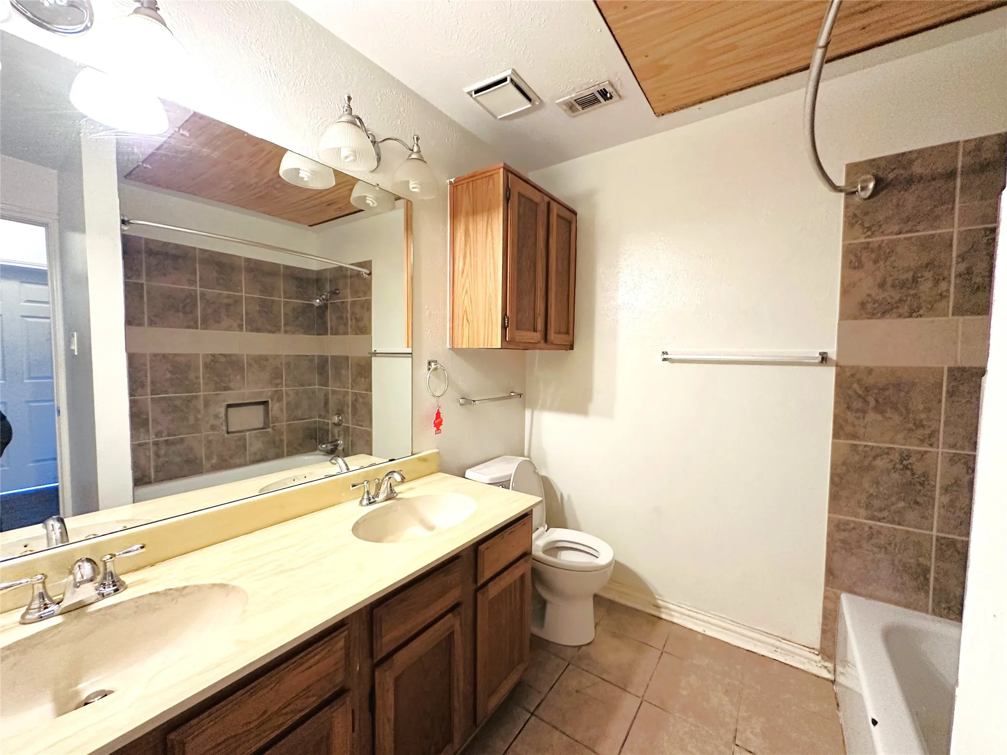Bathroom featuring a dual-sink vanity with wood cabinetry, full-width mirror, and overhead vanity lighting