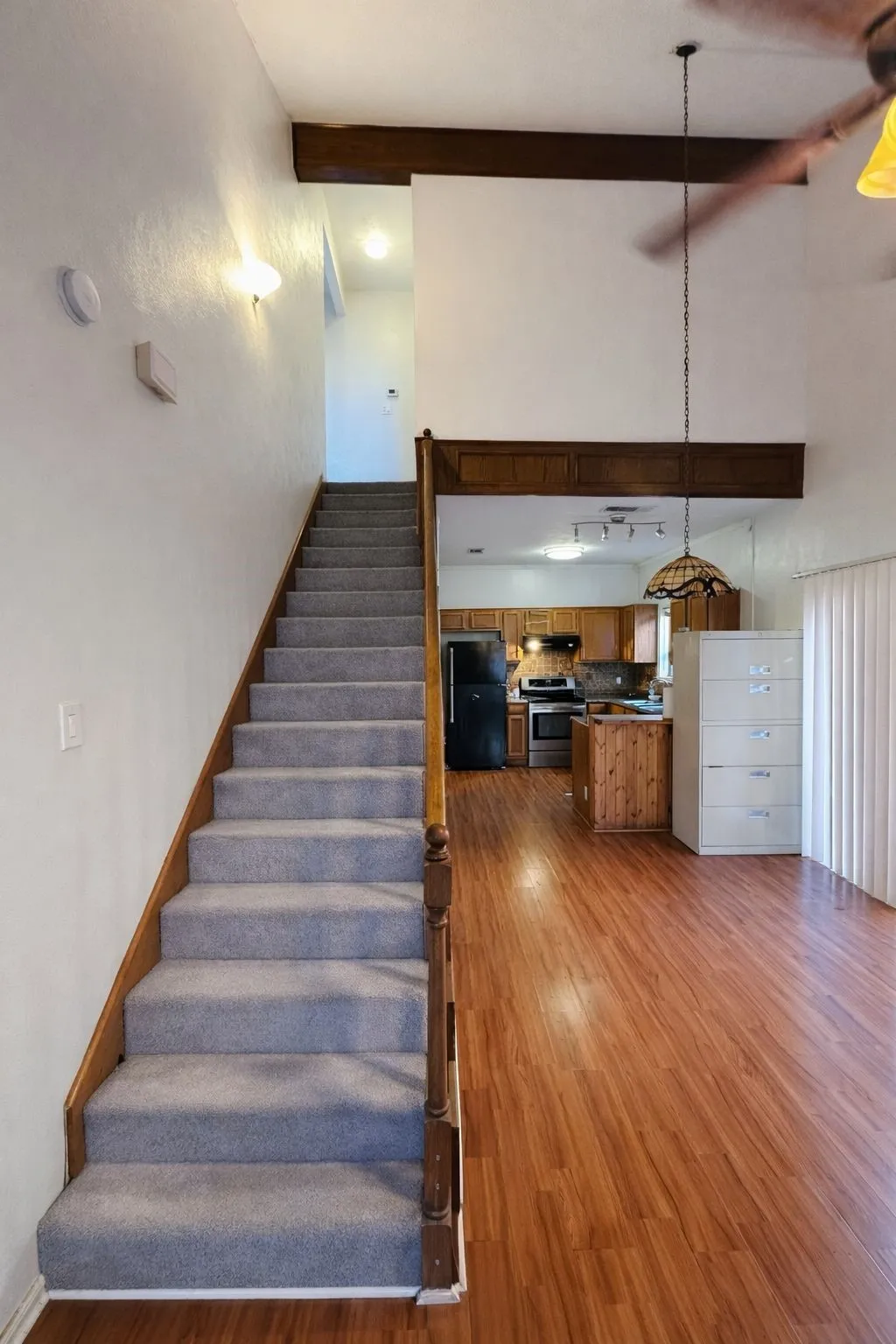 Carpeted staircase with wood banister, wood-finish flooring, and high ceilings with exposed beams