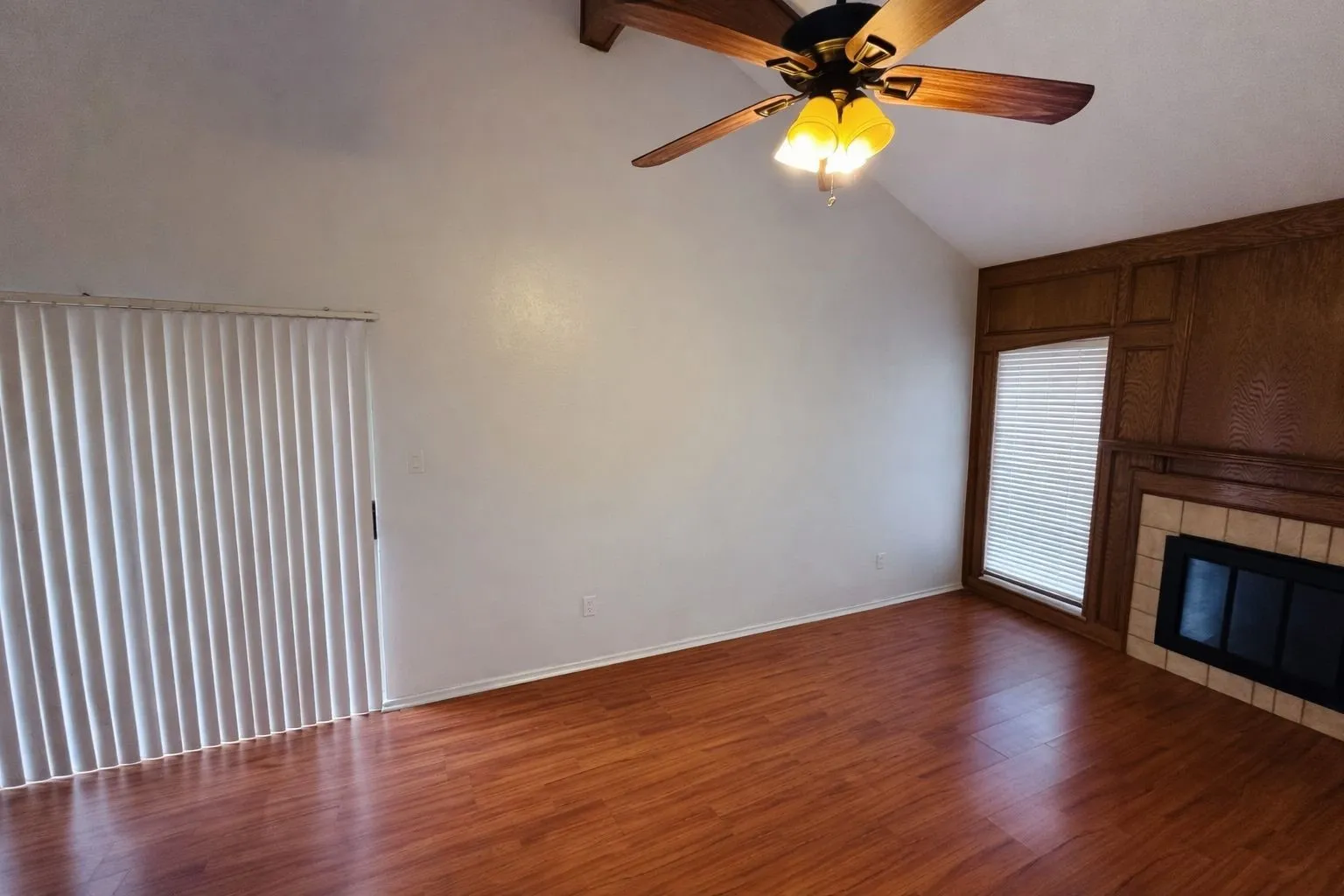 Living area with vaulted ceiling, wood-finish flooring, and a fireplace featuring a tile surround and wood paneling