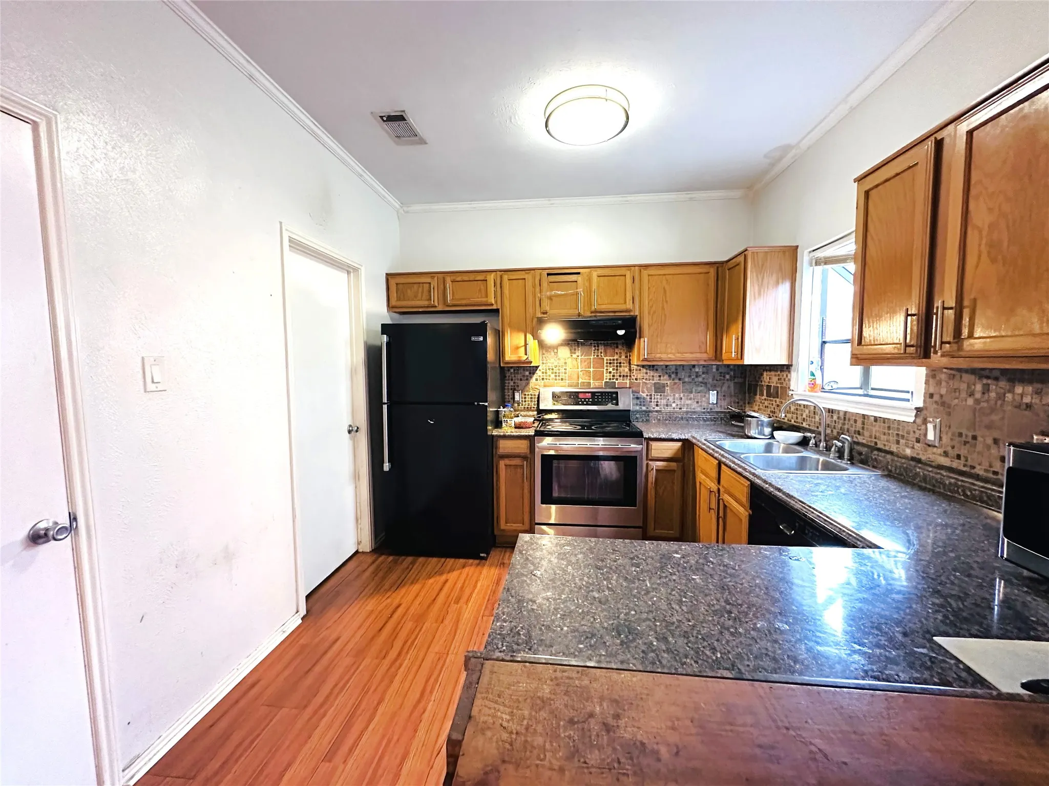 Kitchen featuring wood-finish flooring, oak cabinetry, stainless steel range and microwave, and a dark speckled countertop with a mosaic tile backsplash