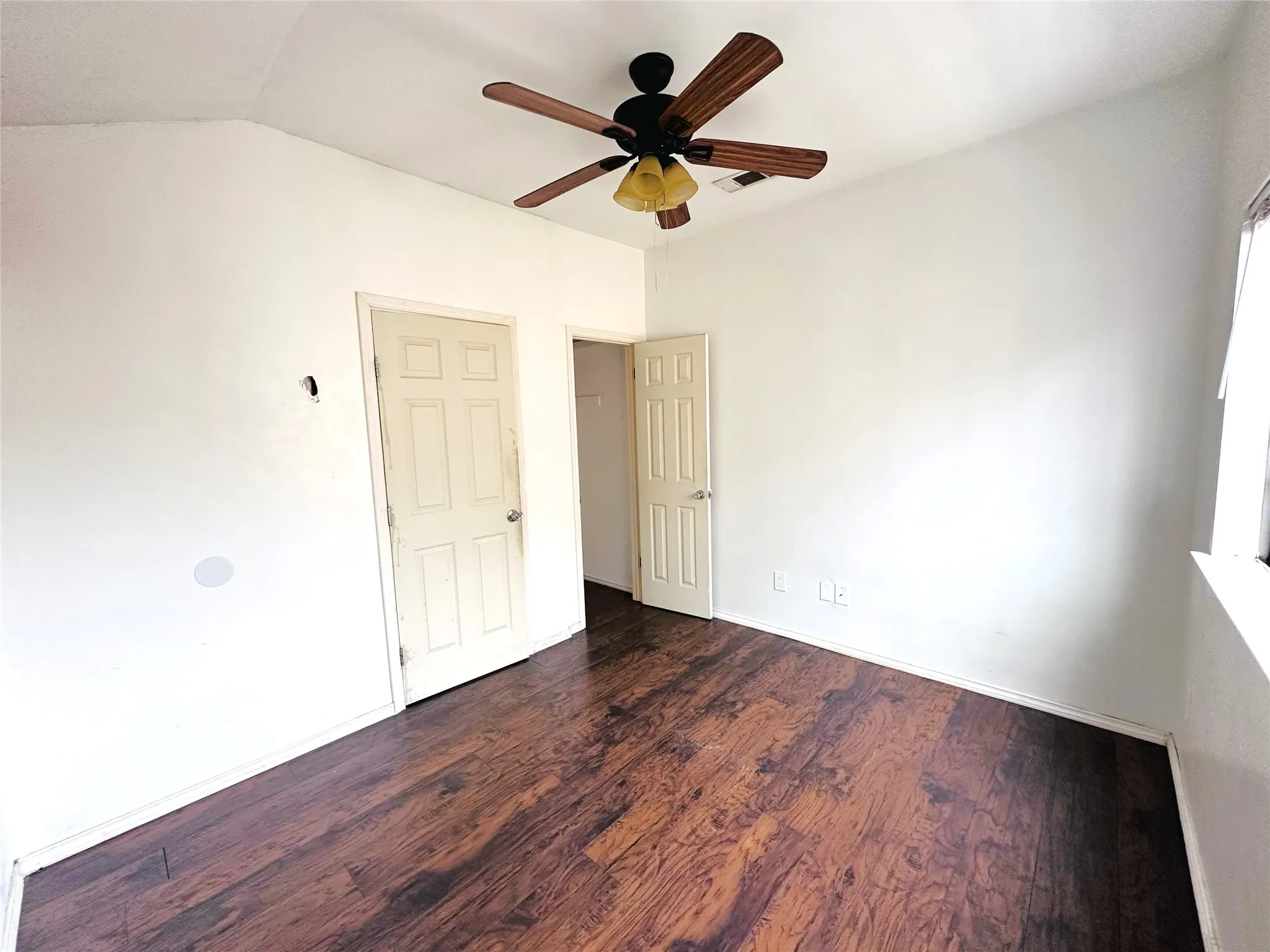 Room featuring wood-finish flooring, a ceiling fan with light fixture, and white painted walls
