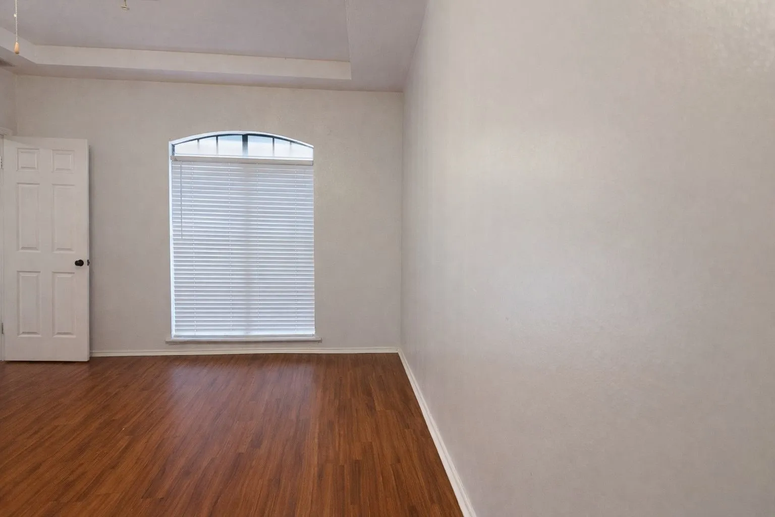 Spacious room featuring wood-finish flooring, an arched window with blinds, and white trim throughout