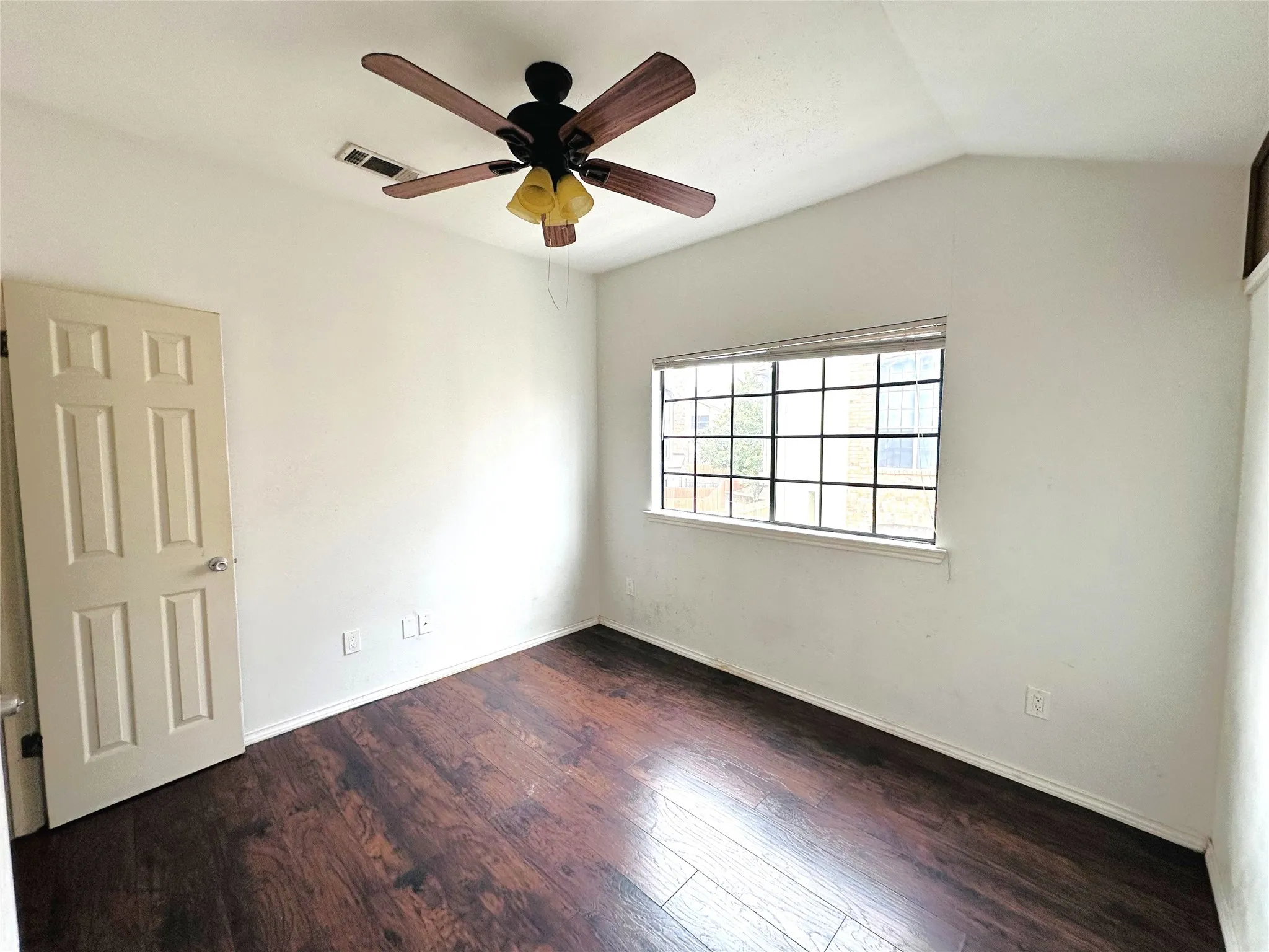 Room featuring wood-finish flooring, a vaulted ceiling, a multi-pane window, and a ceiling fan with integrated lighting