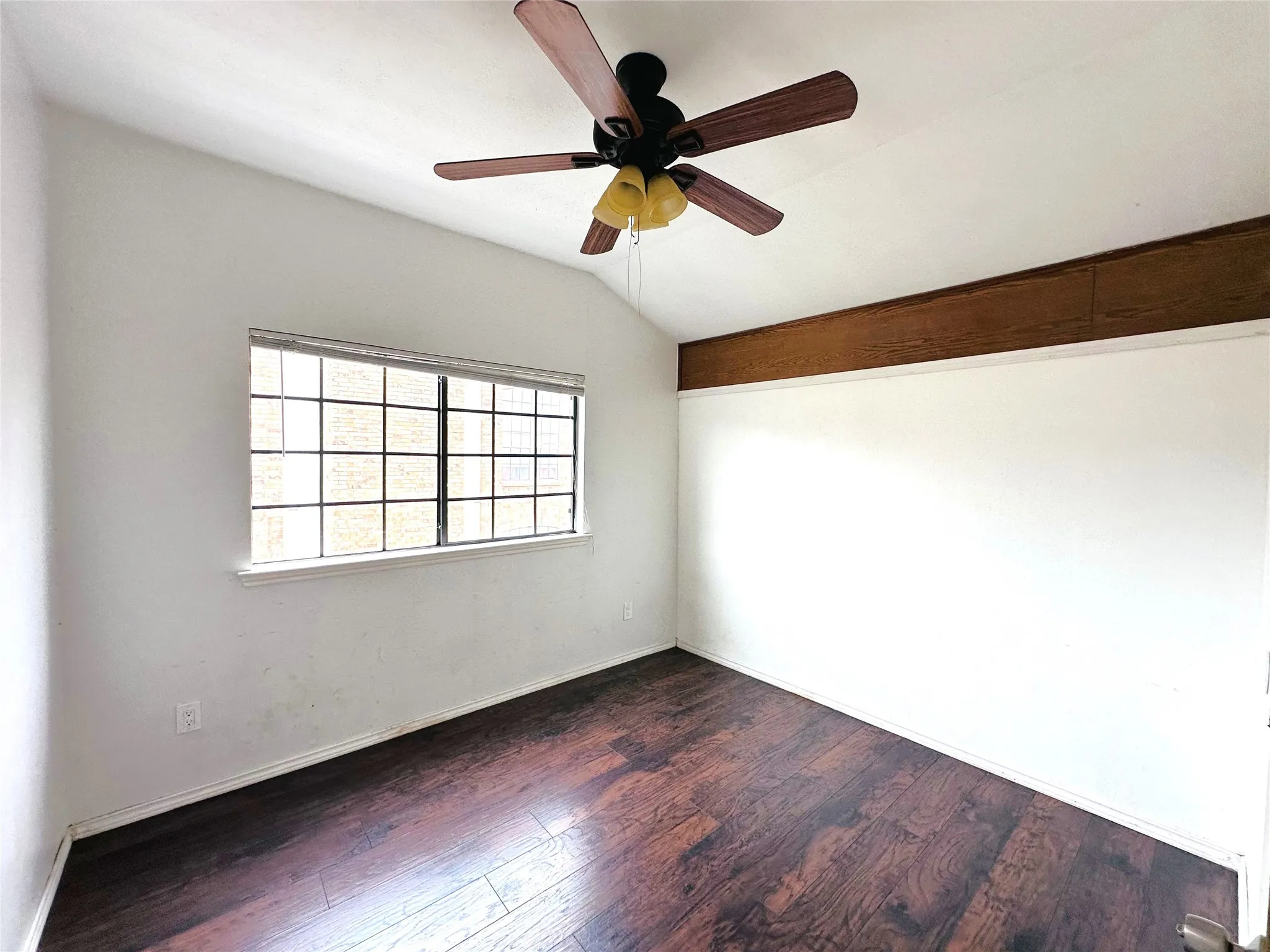 Vaulted ceiling room featuring wood-finish flooring, a ceiling fan with light fixture, and a large window with grid panes