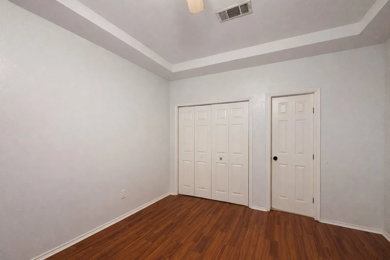 Bedroom featuring wood-finish flooring, a tray ceiling, and neutral wall paint