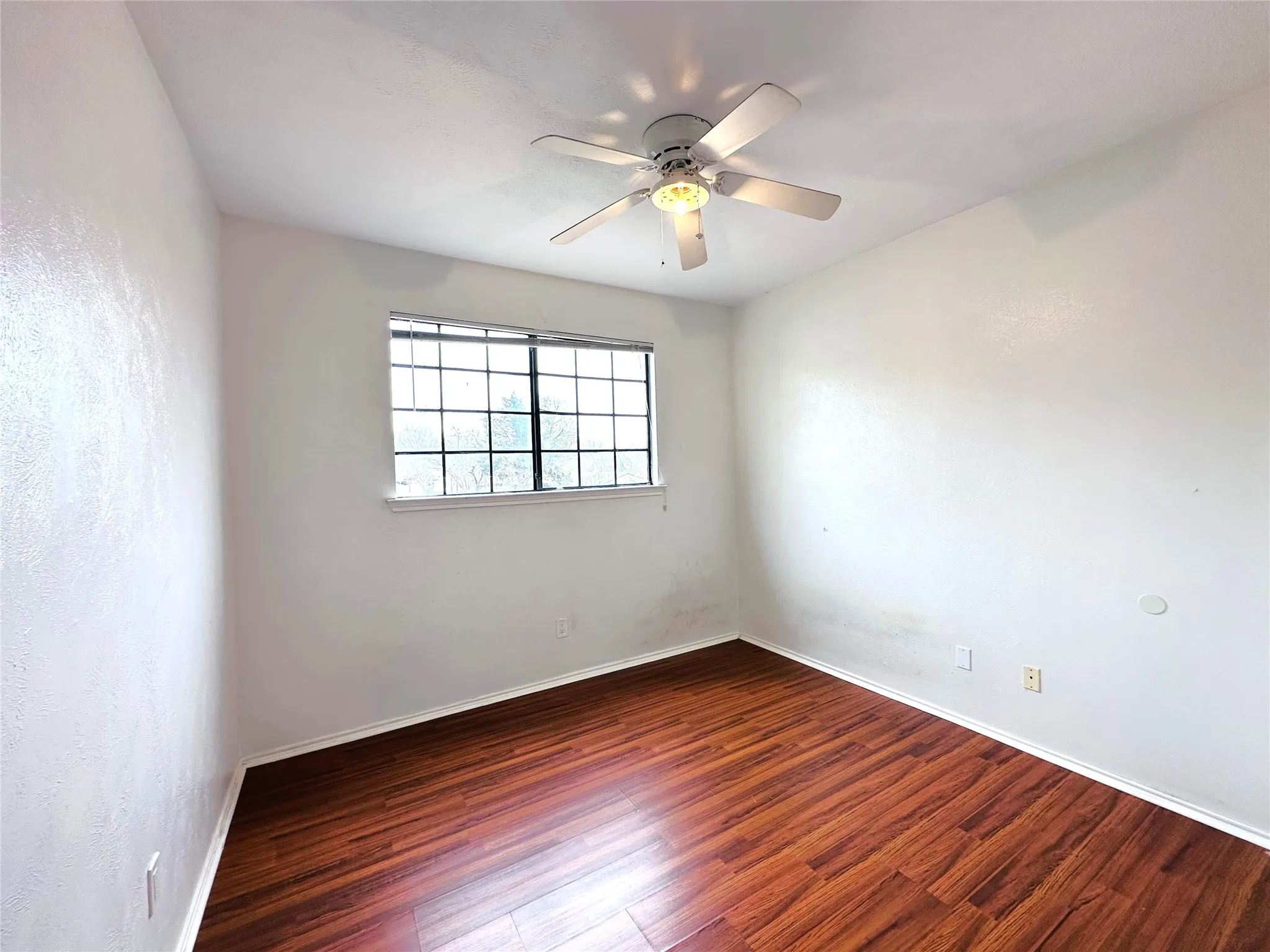 Room featuring wood-finish flooring, a multi-pane window, and a ceiling fan with integrated lighting