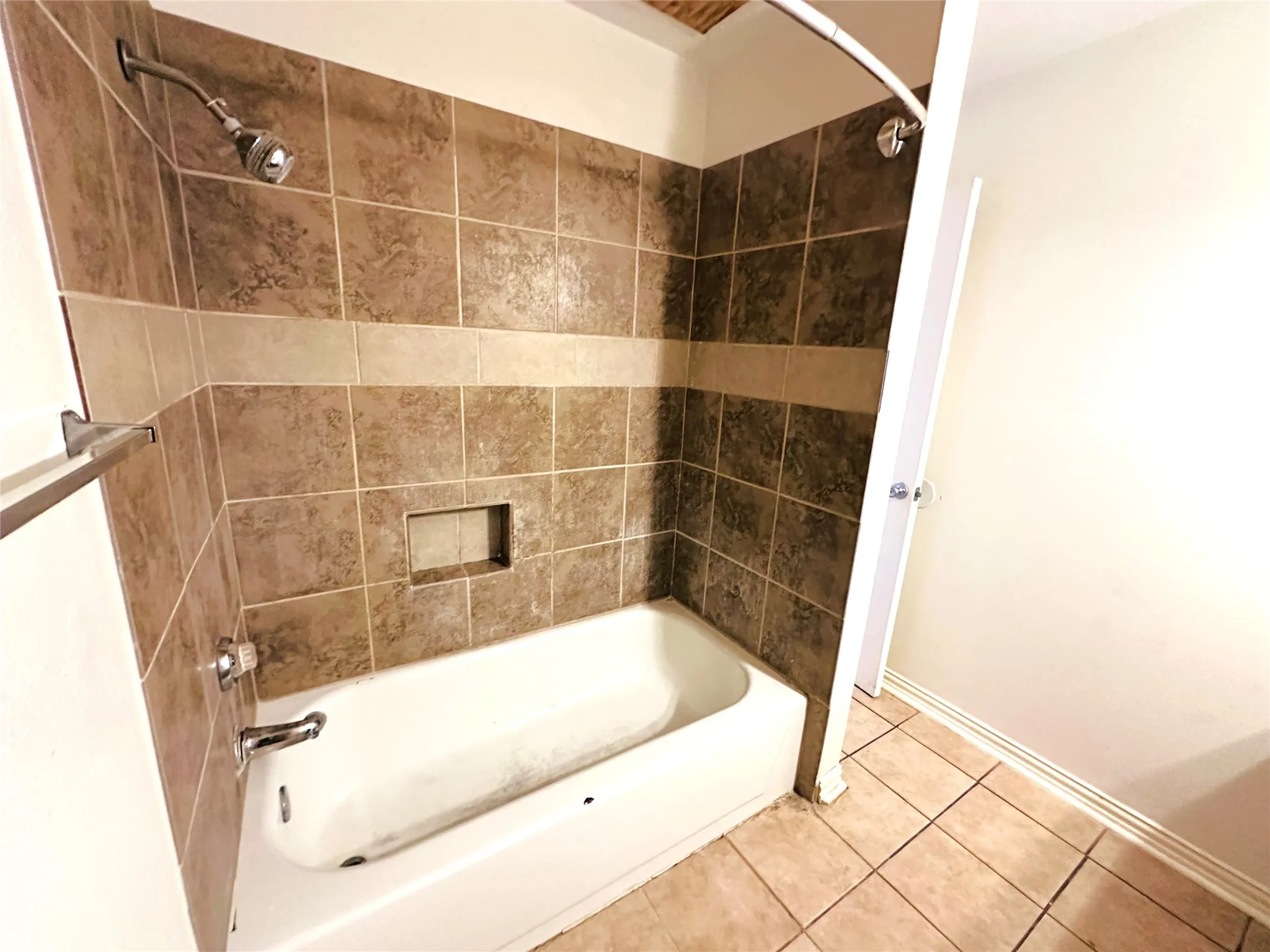 Bathtub with a tiled surround featuring a decorative accent band and integrated niche