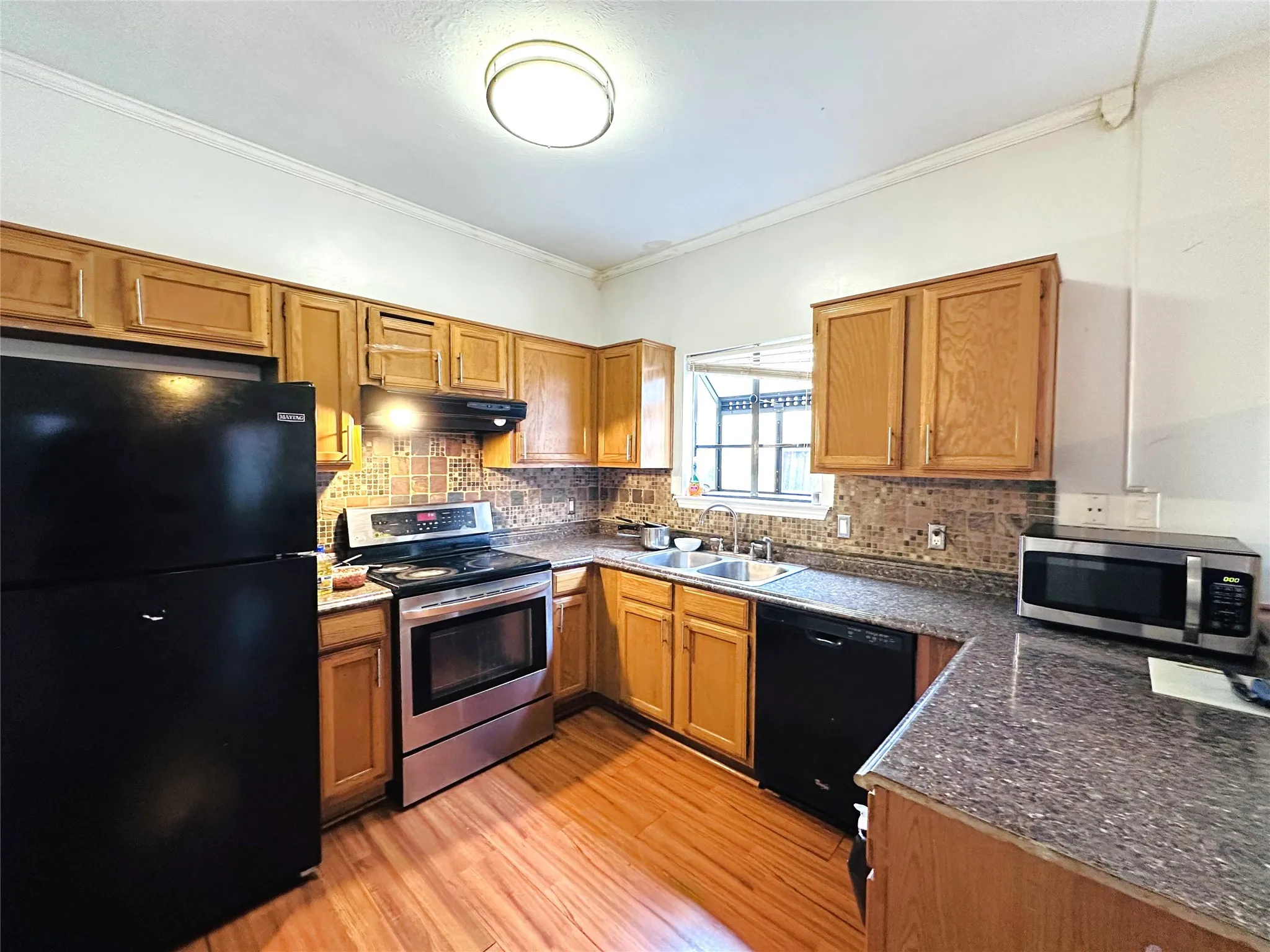 Kitchen featuring wood-finish flooring, natural wood cabinetry, and a mosaic tile backsplash