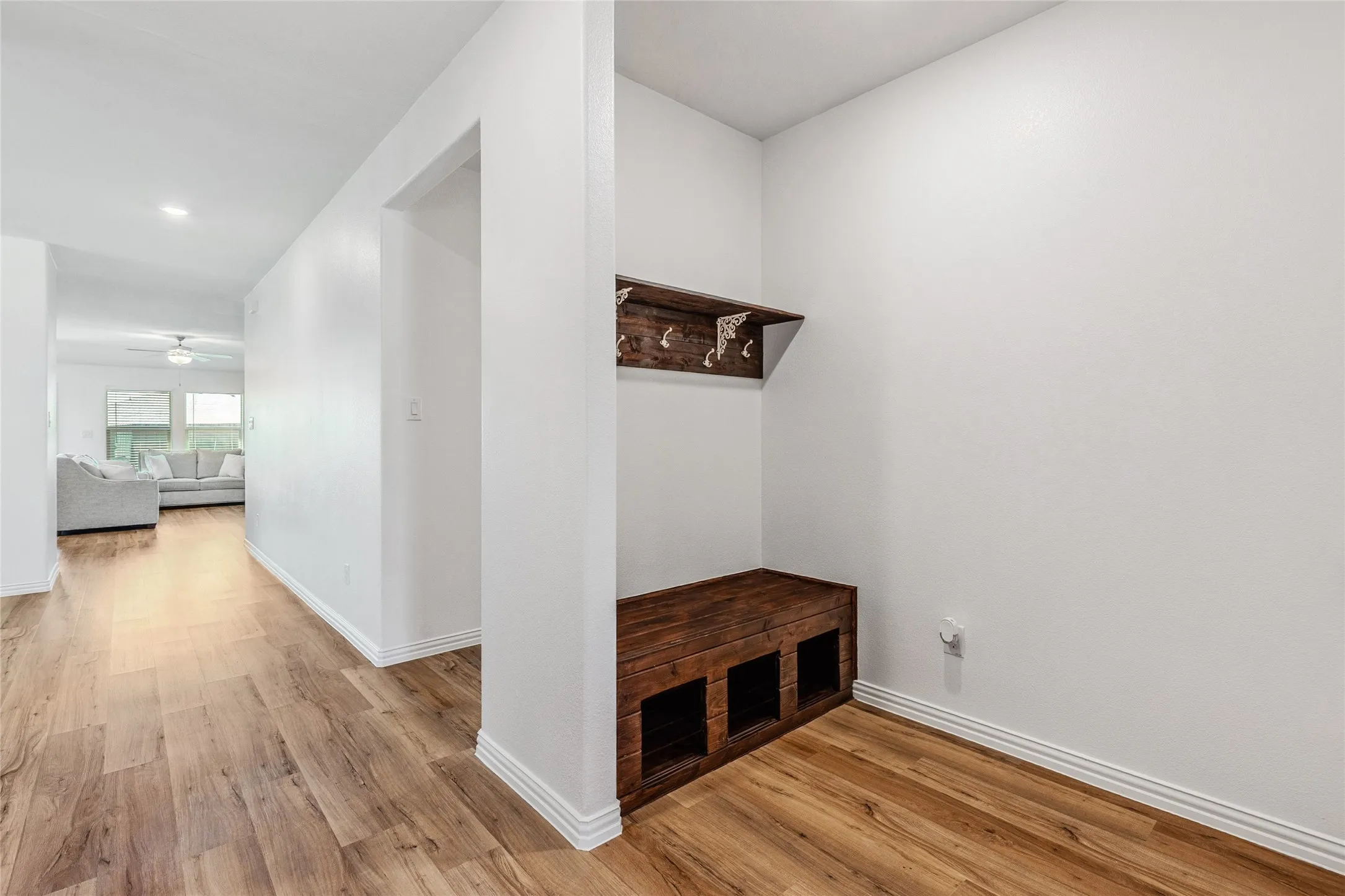 Entryway with wood-finish flooring, white baseboards, and a built-in wooden bench with storage cubbies and an overhead shelf with hooks