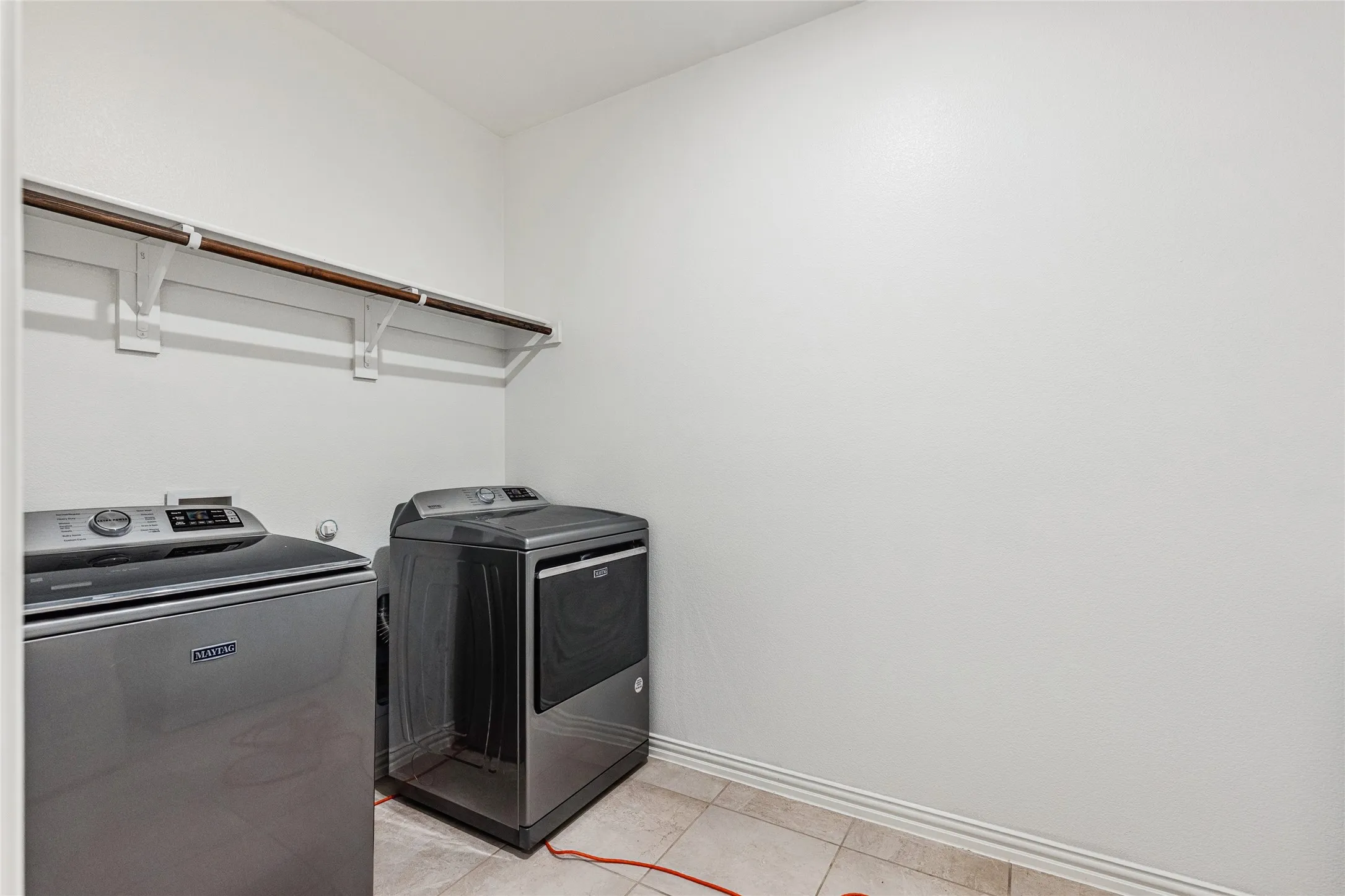 Utility area with light tile flooring, white walls, and a built-in shelving and hanging rod system