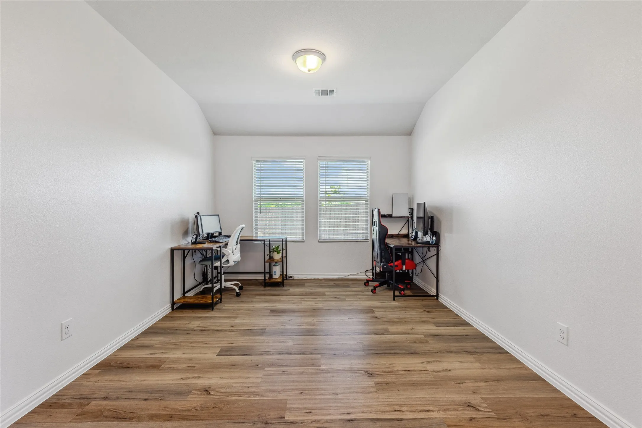 Spacious room featuring wood-finish flooring, white walls, and two windows with horizontal blinds