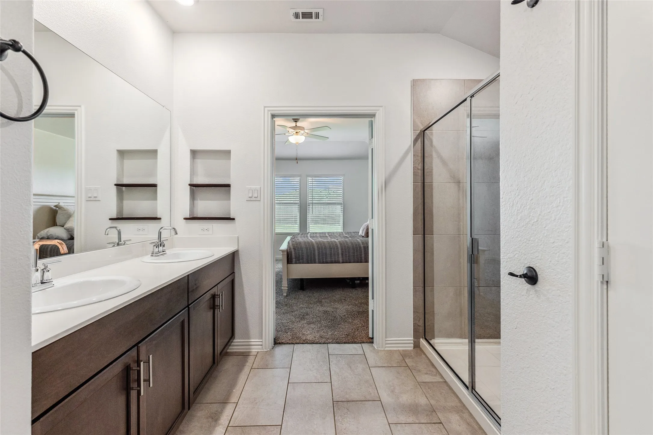 Bathroom featuring a dual vanity with undermount sinks, quartz-finish countertop, dark wood-finish cabinetry, and a glass-enclosed shower