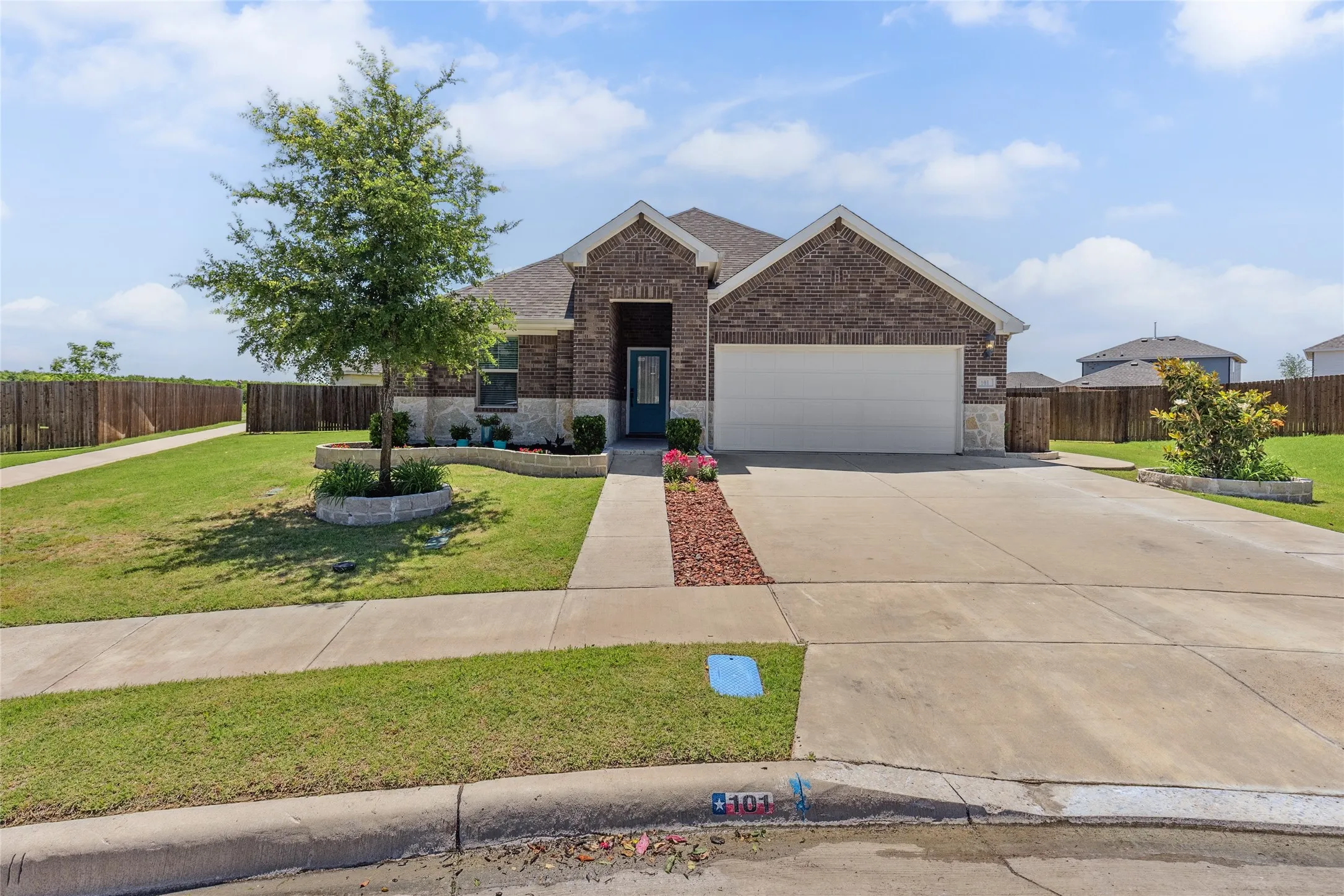 Brick and stone facade residence featuring a two-car garage, concrete driveway, front walkway, and perimeter wood fencing