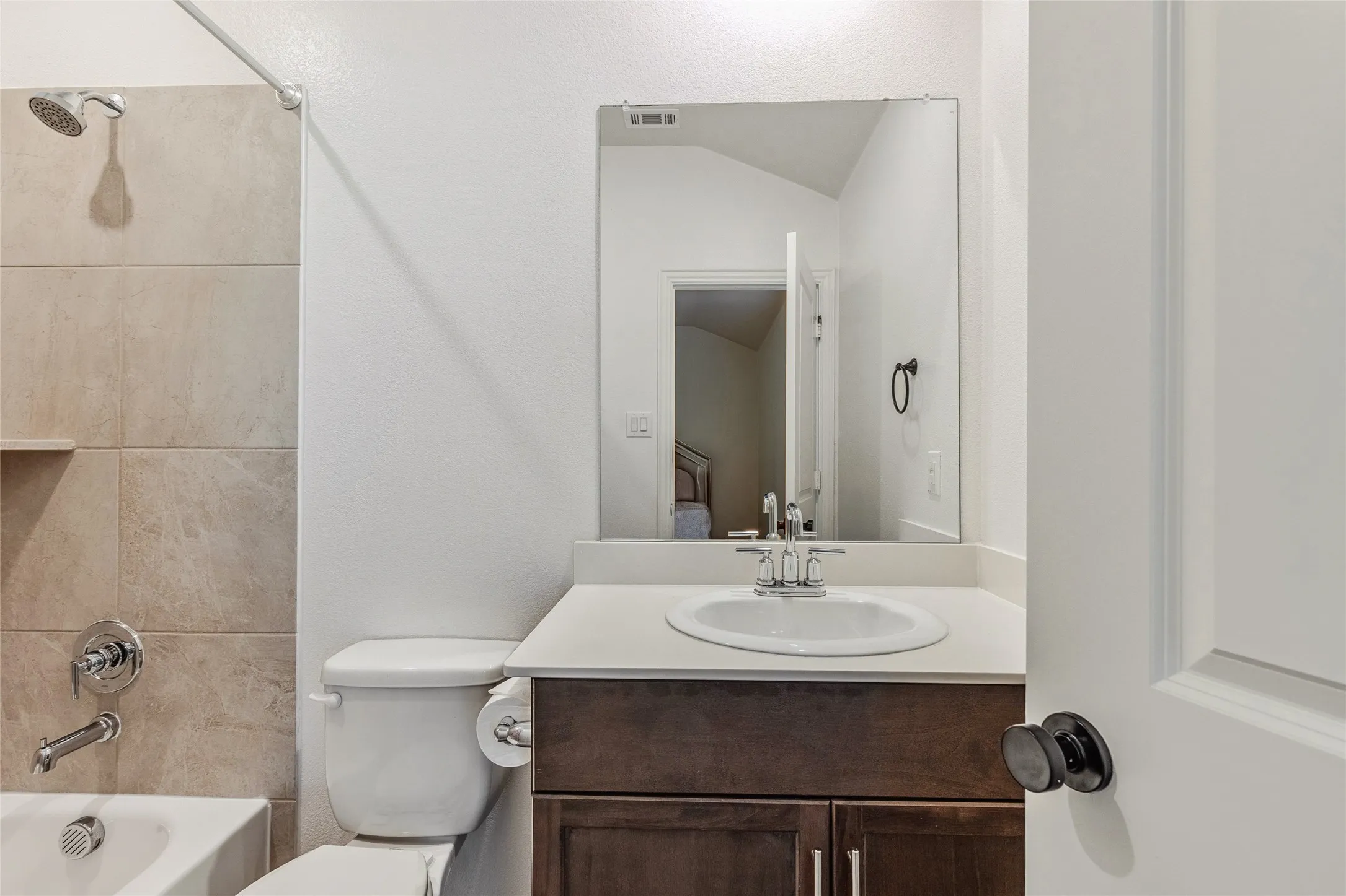 Full bathroom featuring a tub and shower combination with light-toned tile surround, a single vanity with a white countertop and integrated sink, and dark wood-finish cabinetry