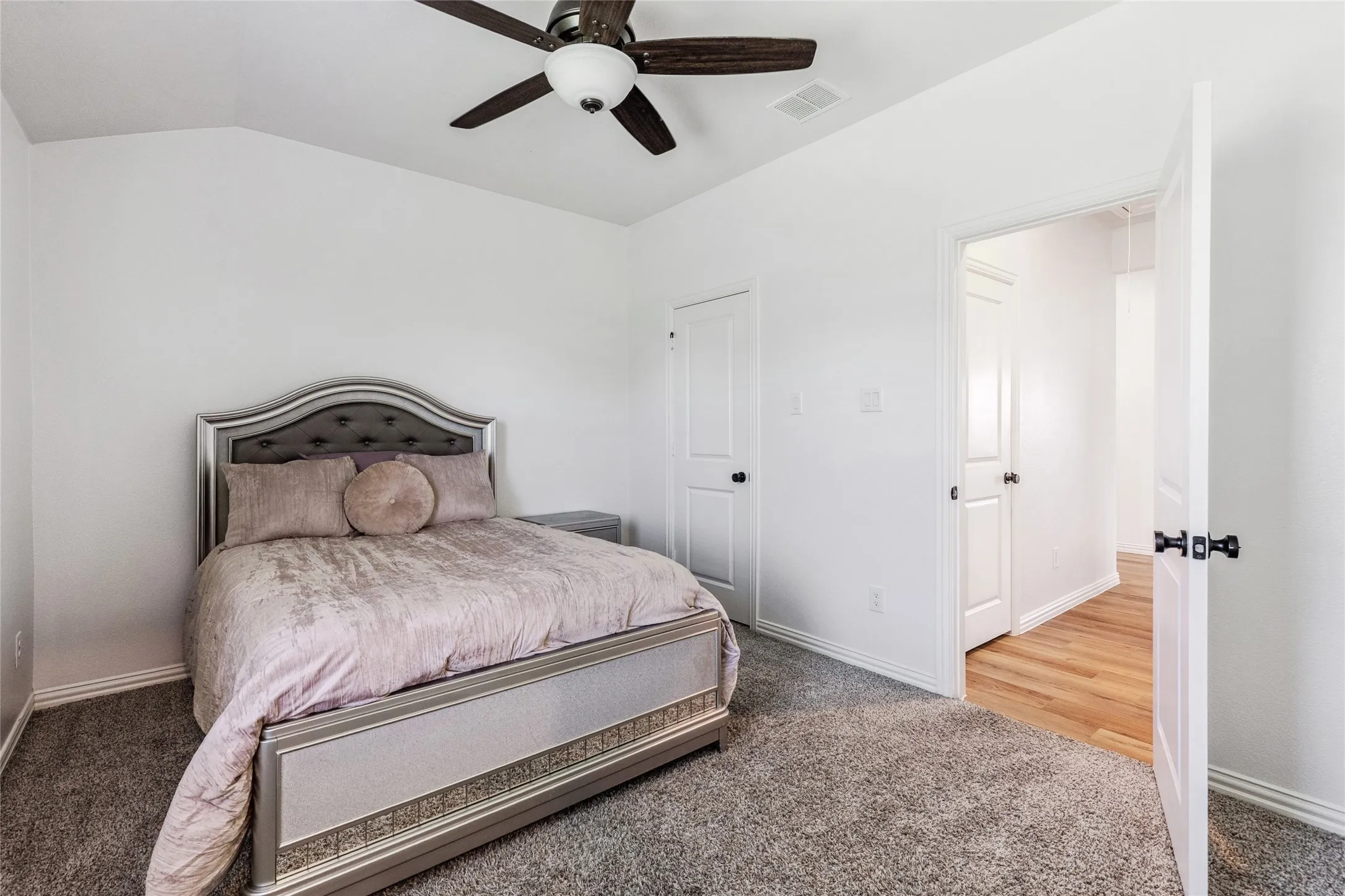 Carpeted interior room featuring a ceiling fan with integrated lighting, a white painted door with black hardware, and an additional white painted door