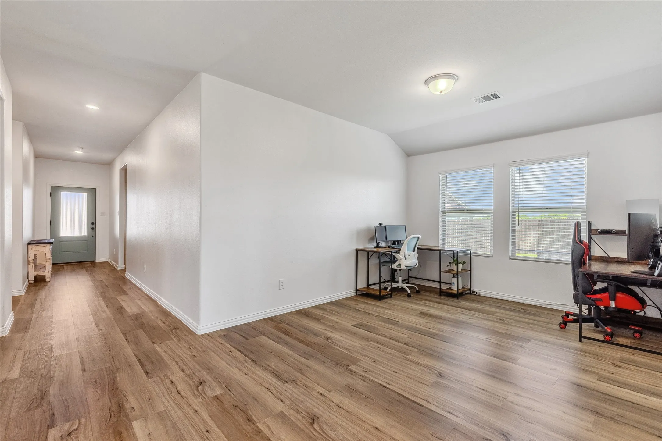 Spacious interior room featuring wood-finish flooring, white walls, and a semi-flush ceiling light fixture