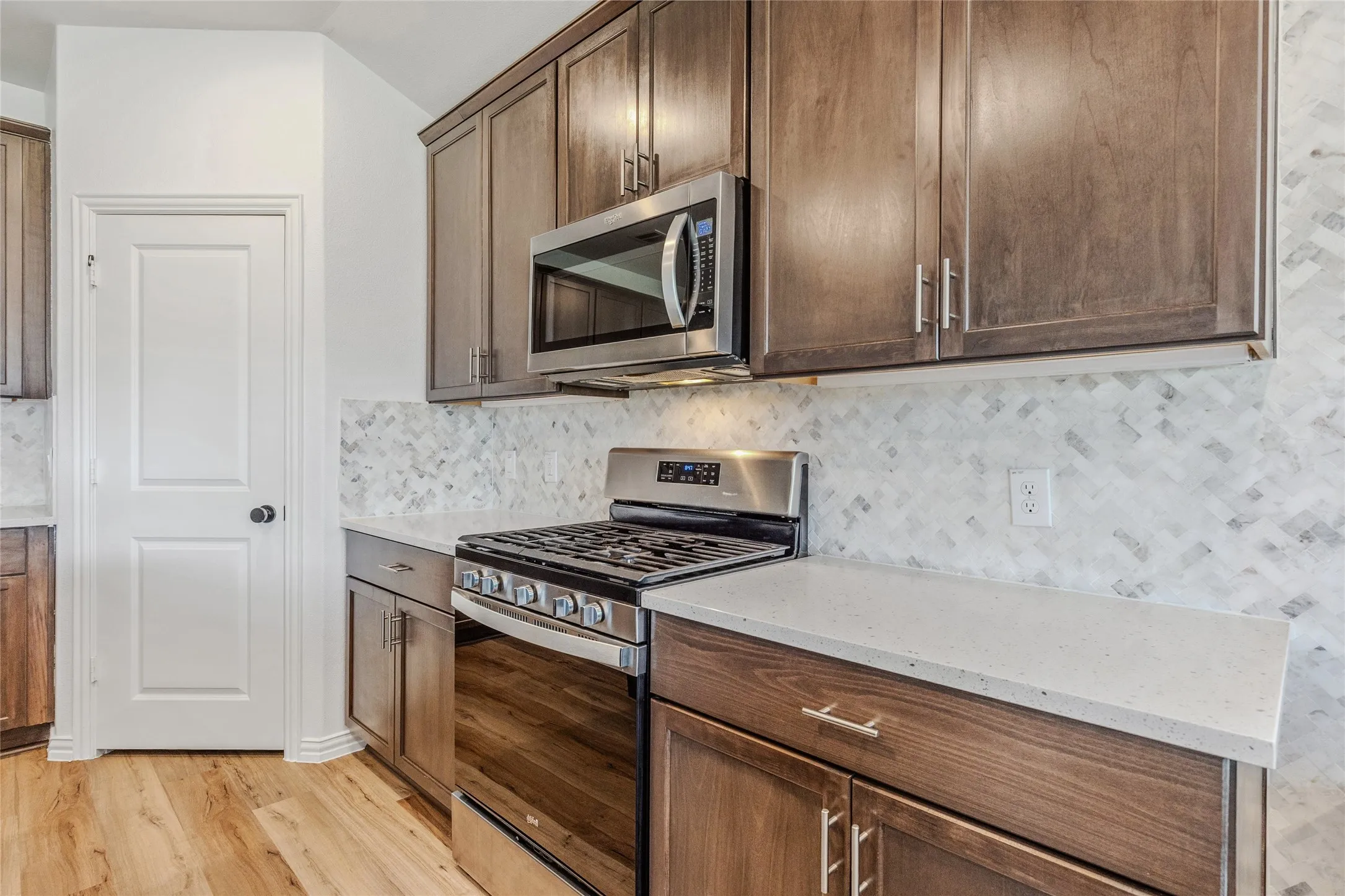 Kitchen featuring stainless steel appliances, wood-finish cabinetry, quartz countertops, and a herringbone-patterned tile backsplash