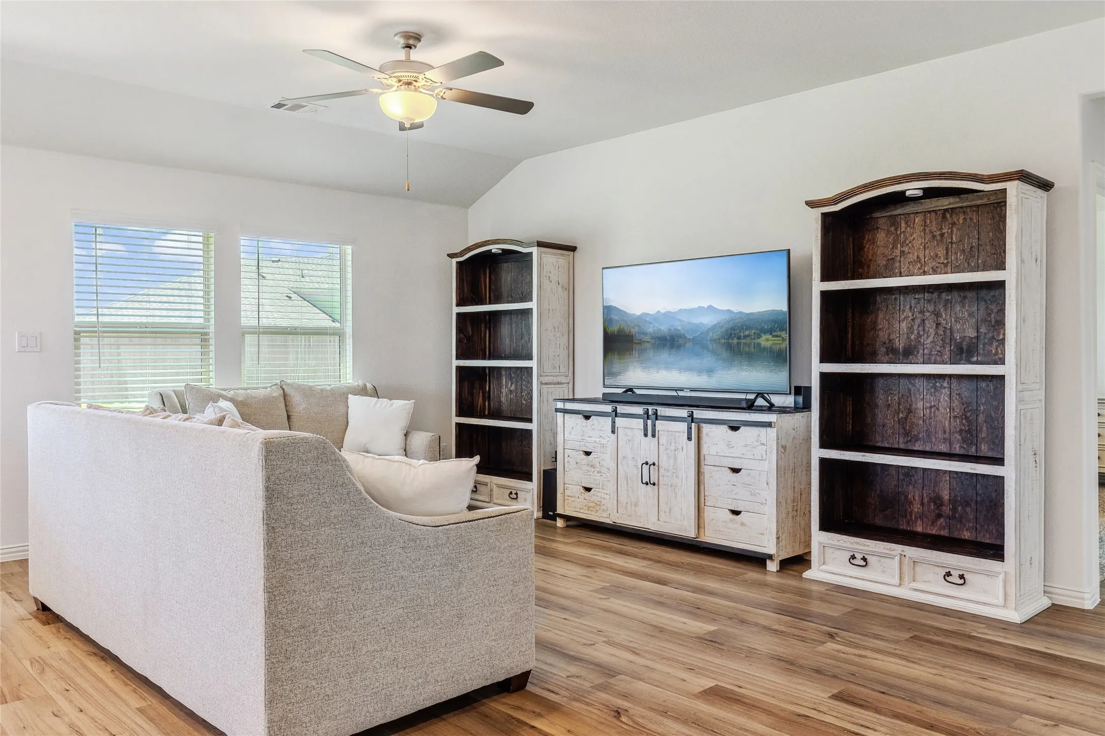 Spacious living area featuring wood-finish flooring, ample natural light from multiple windows, and a ceiling fan with integrated lighting