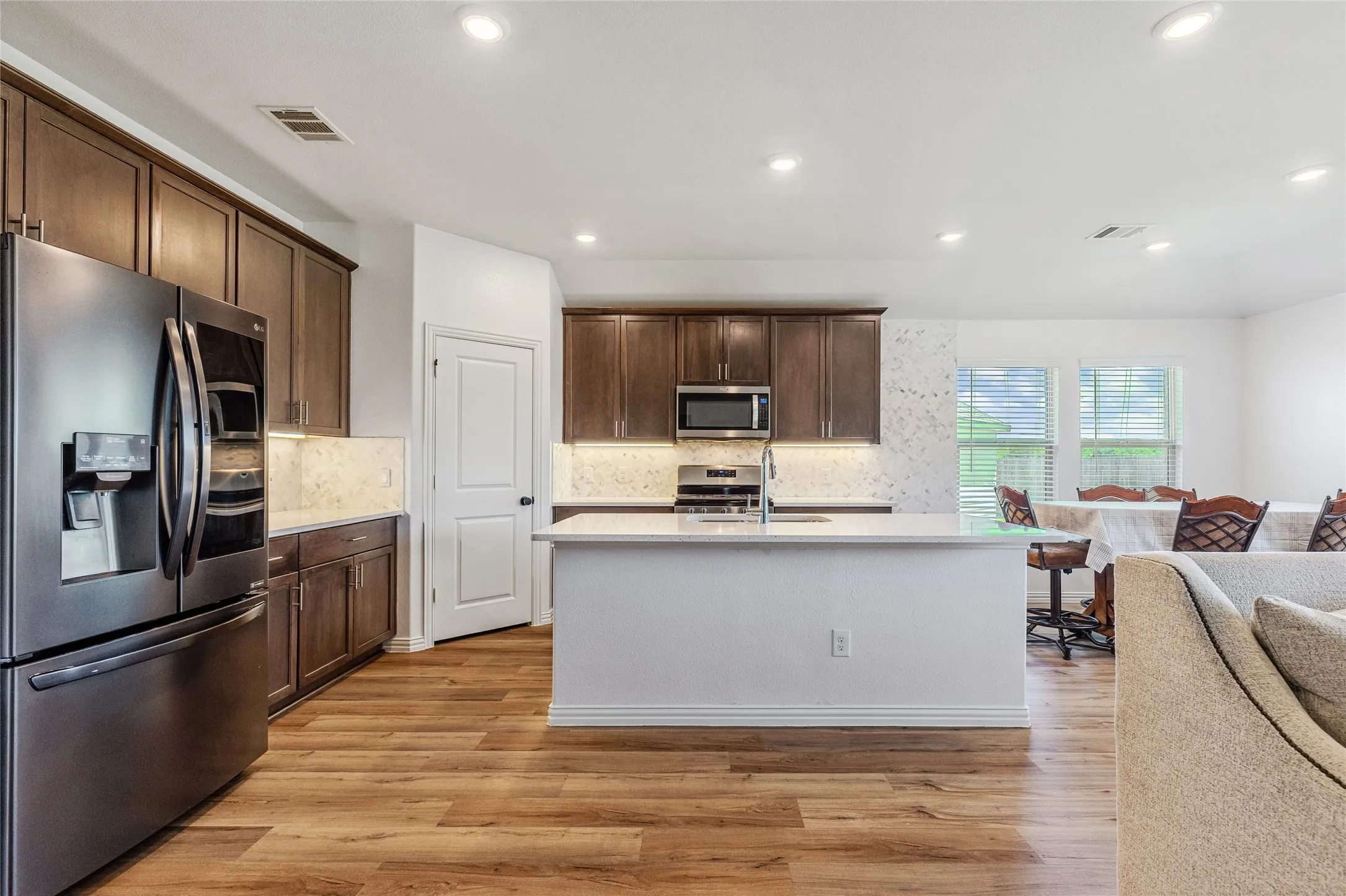 Spacious kitchen featuring wood-finish flooring, dark wood cabinetry, light-toned countertops, and a full suite of stainless steel appliances