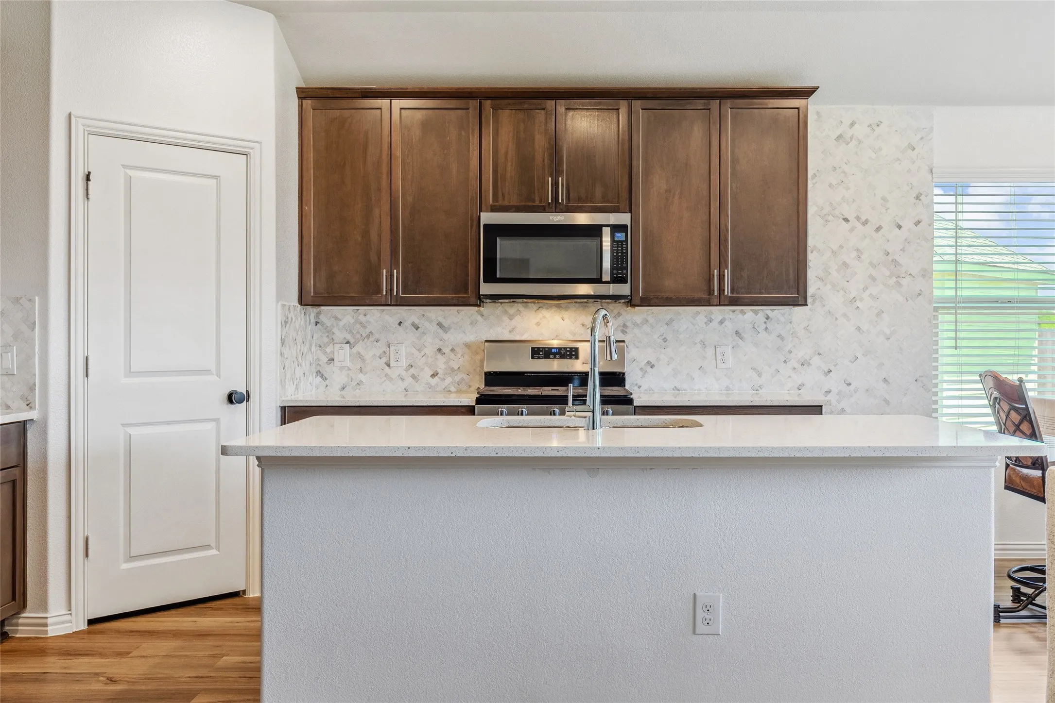 Kitchen featuring a center island, wood-finish flooring, dark wood cabinetry, stainless steel appliances, and a mosaic tile backsplash