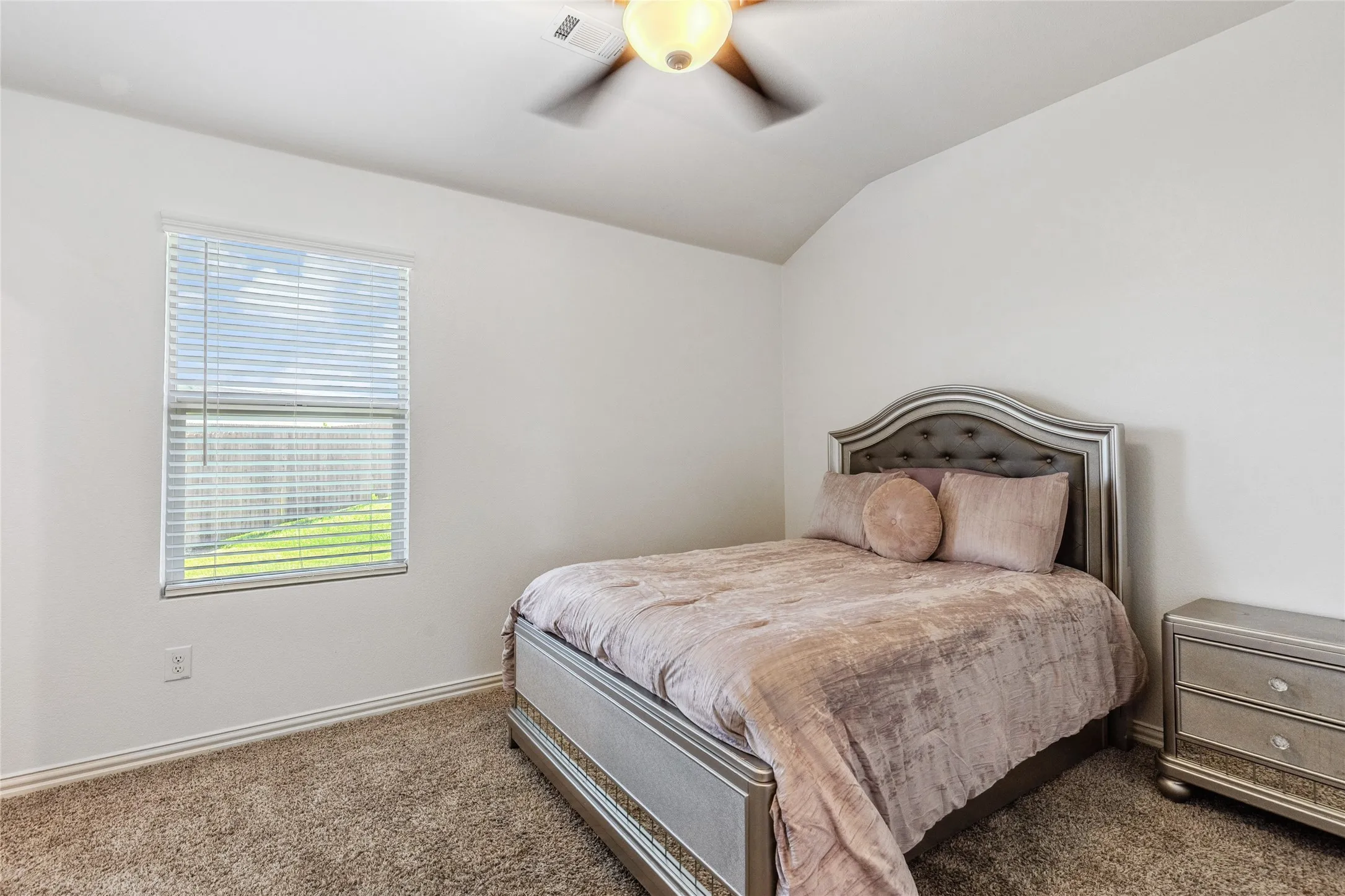 Carpeted room featuring a single window with blinds, a ceiling fan with integrated lighting, white walls, and a vaulted ceiling