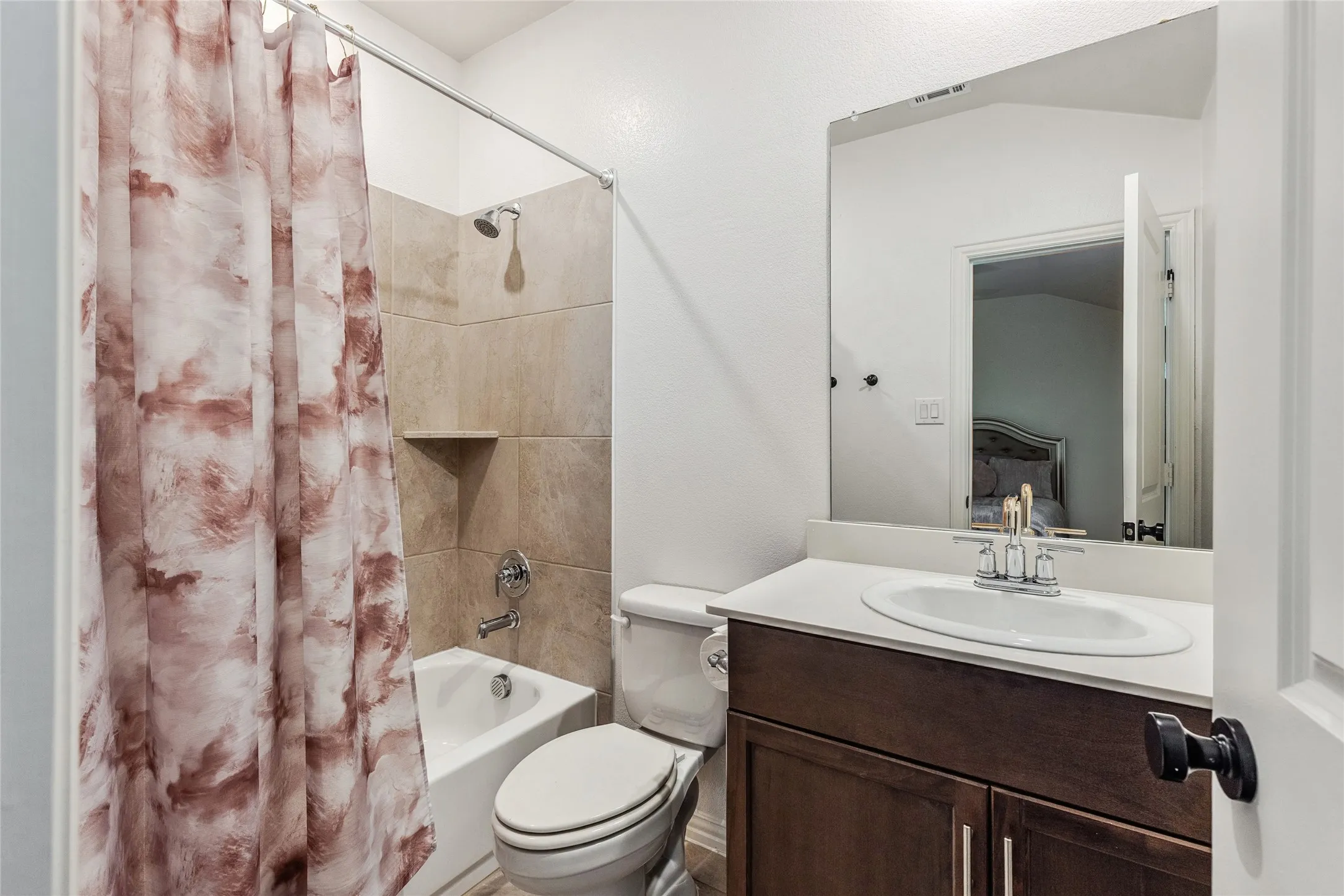 Bathroom featuring a shower-over-tub combination with tiled surround, a built-in shower niche, a single-sink vanity with a dark wood-finish cabinet, and a wall-mounted mirror