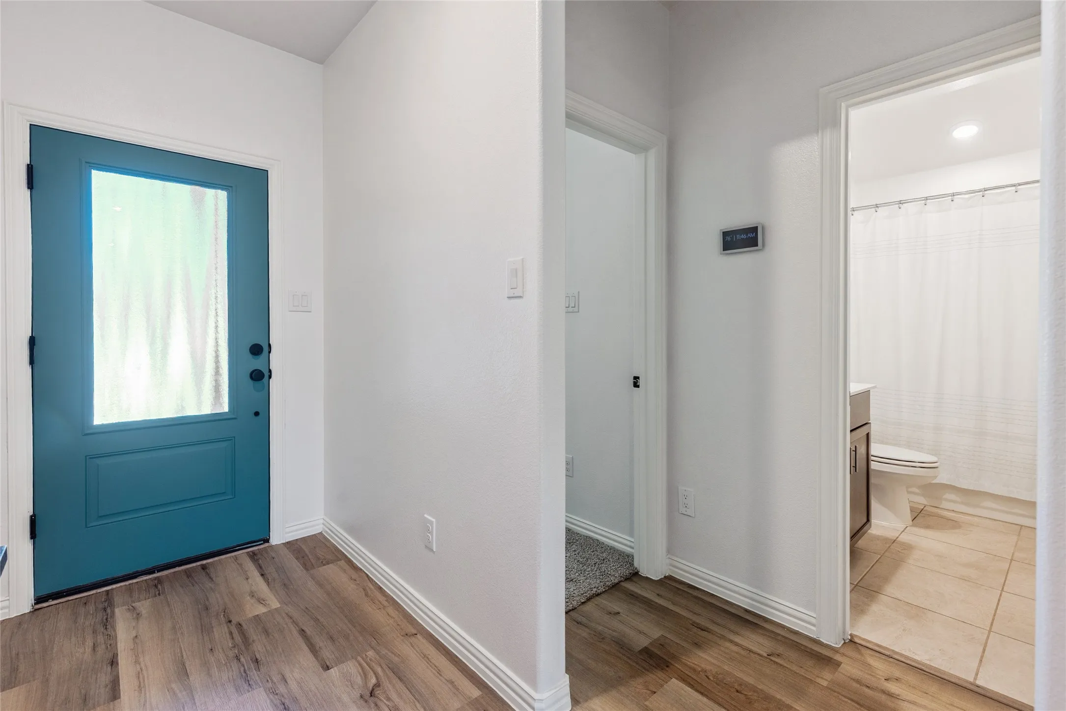 Entryway featuring a vibrant teal door with obscured glass panel, wood-finish flooring, and white baseboards