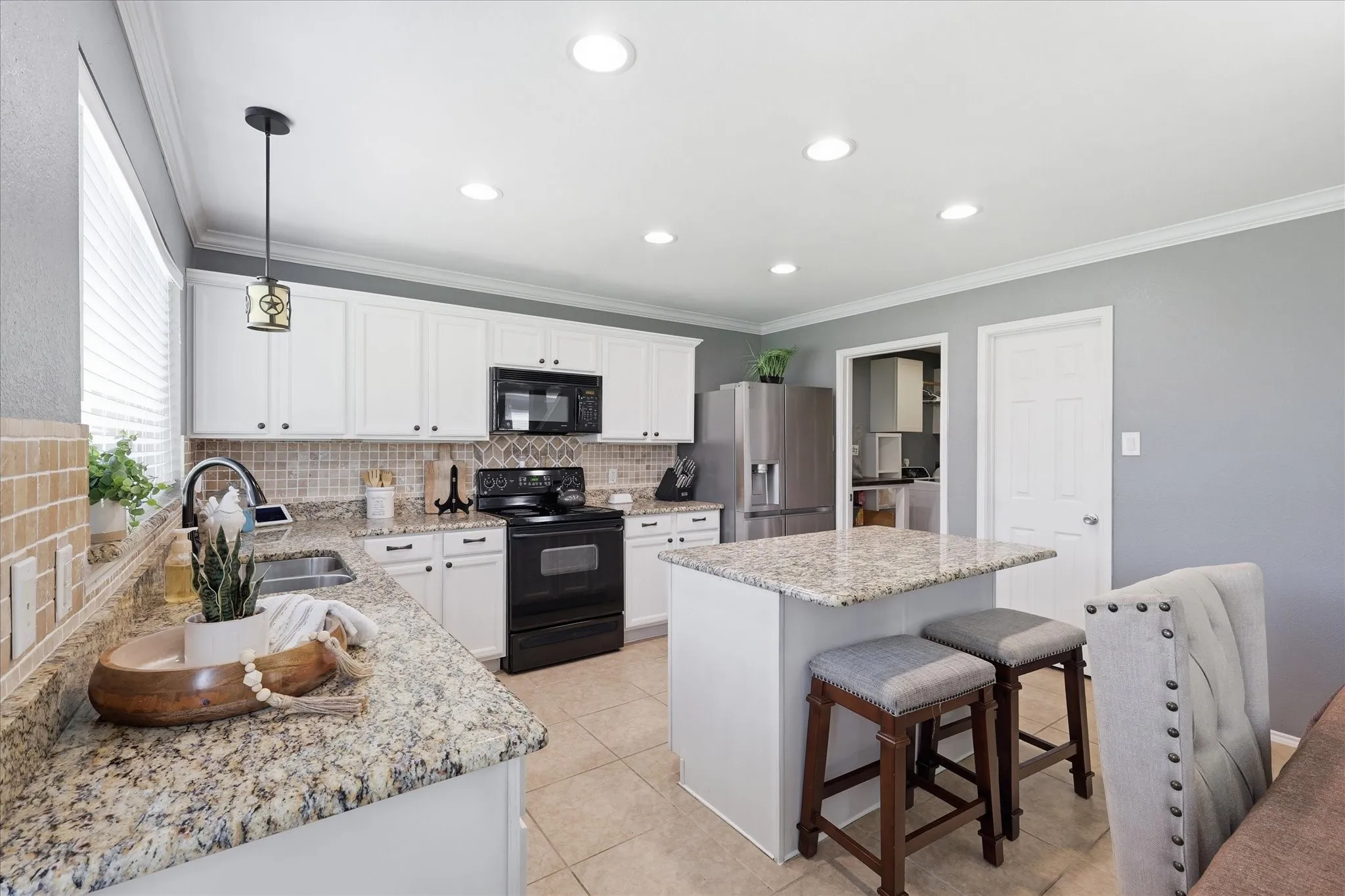 Kitchen featuring white cabinetry, speckled countertops, stainless steel refrigerator, black range, and an island with seating