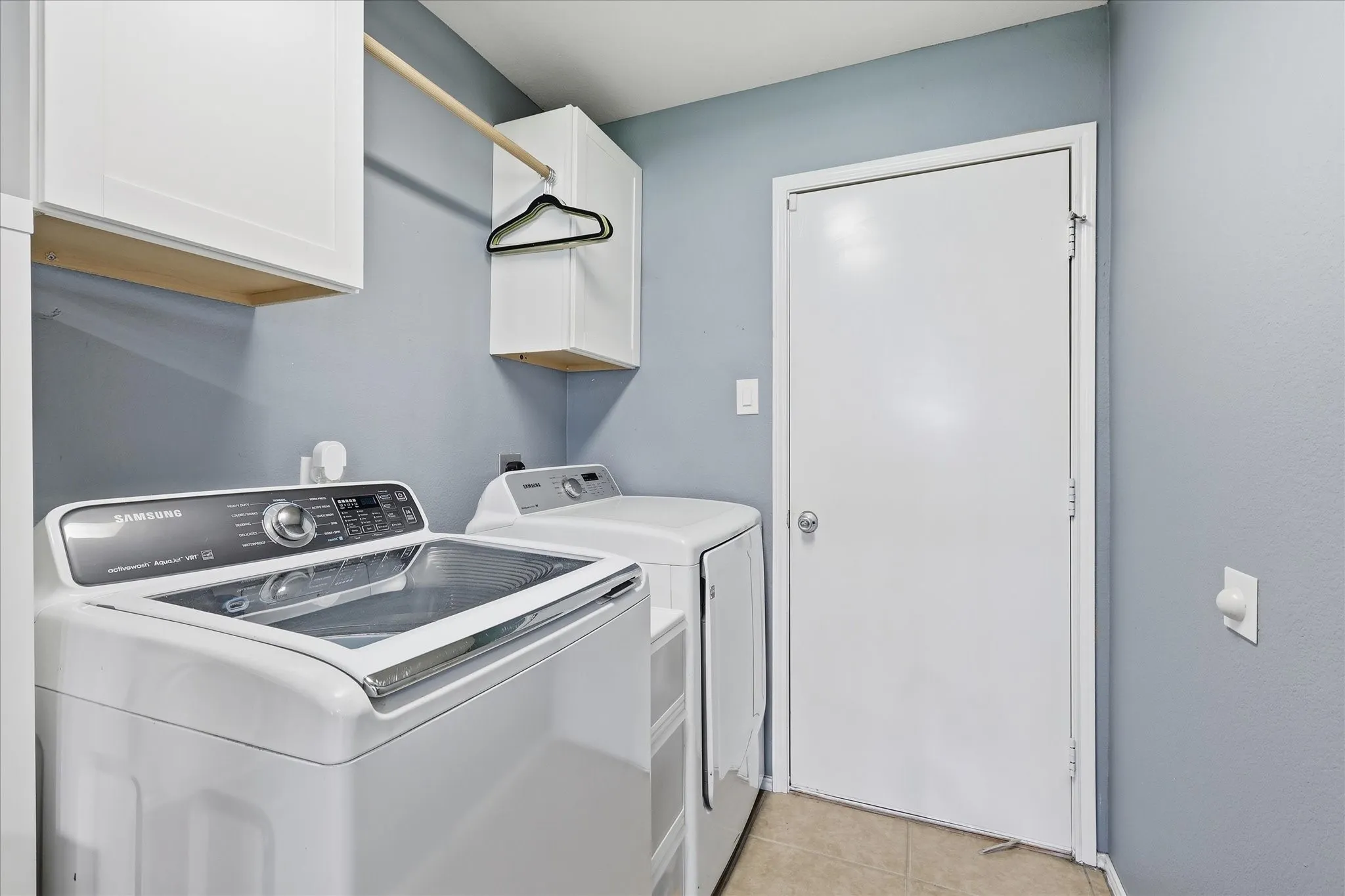 Dedicated laundry area featuring white upper cabinetry, a wood-finish hanging rod, and light tile flooring