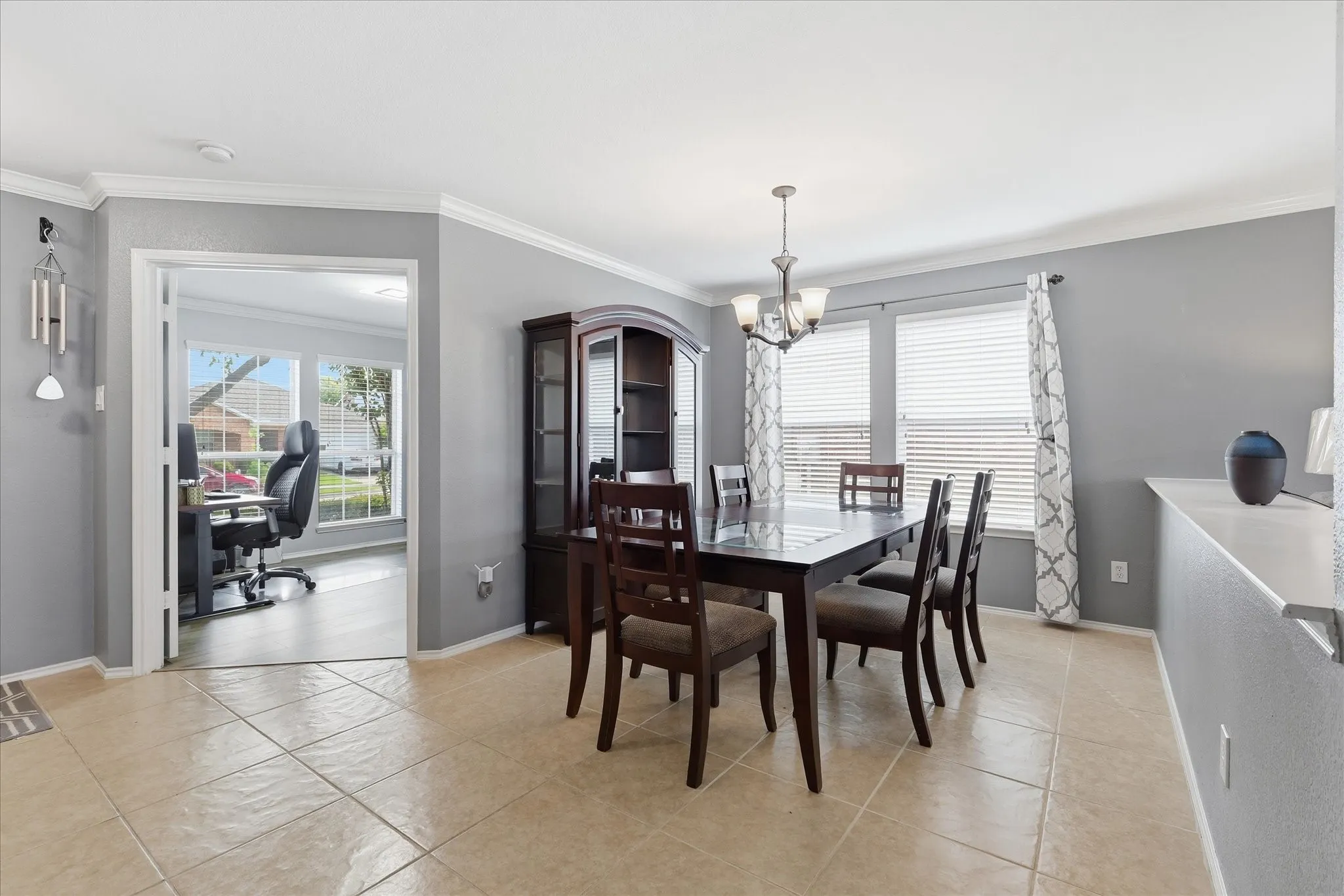 Spacious dining area featuring neutral-toned tile flooring, gray walls, and white crown molding