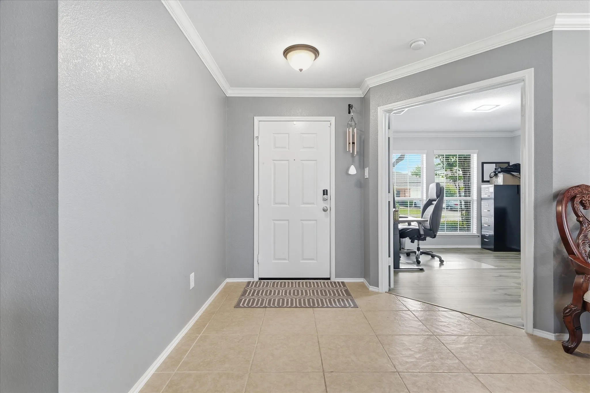 Entryway featuring tile flooring, white crown molding, a panel door with a smart lock, and an overhead lighting fixture