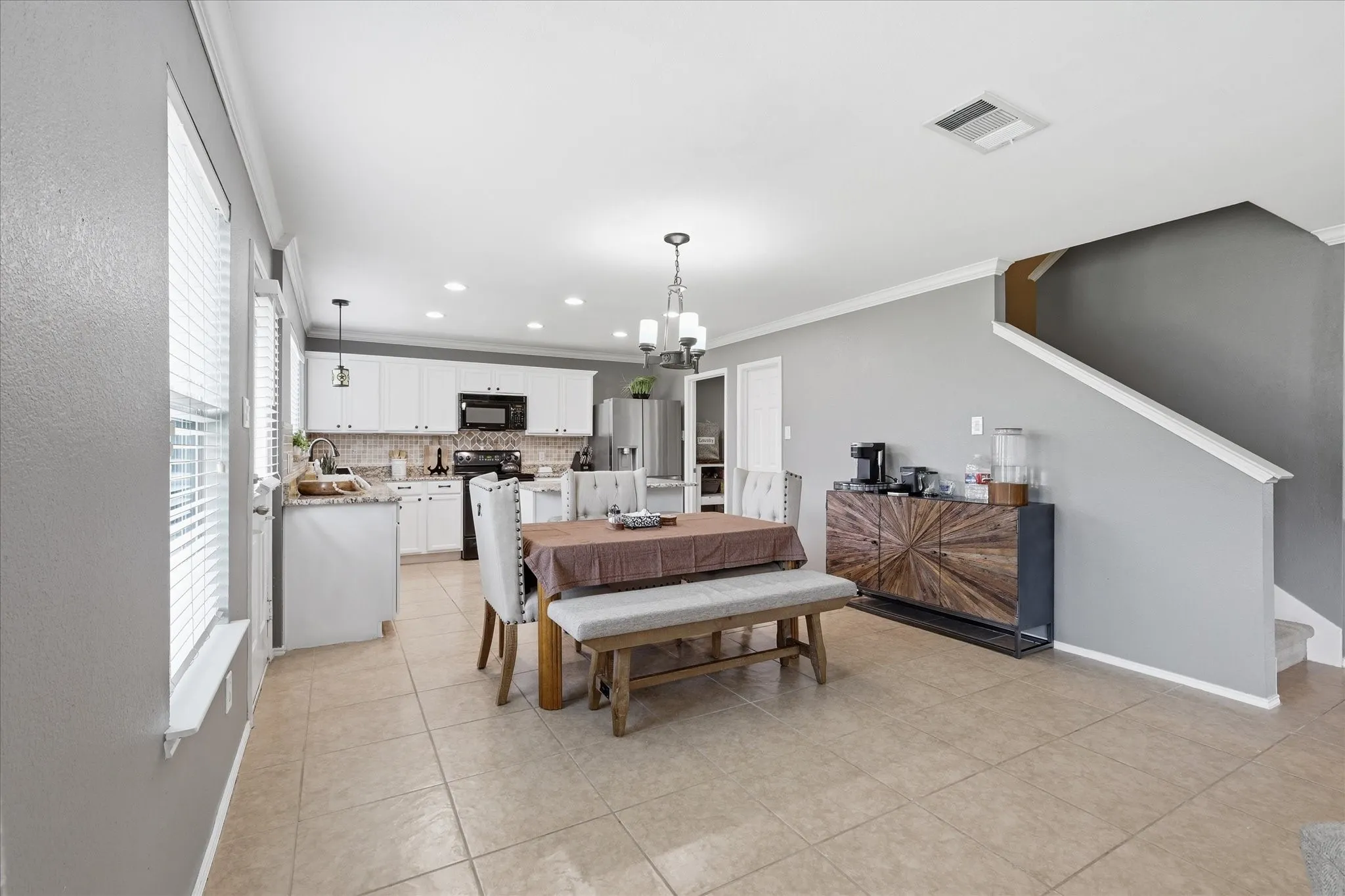 Open-concept kitchen and dining area featuring white cabinetry, tile flooring, and a contemporary chandelier